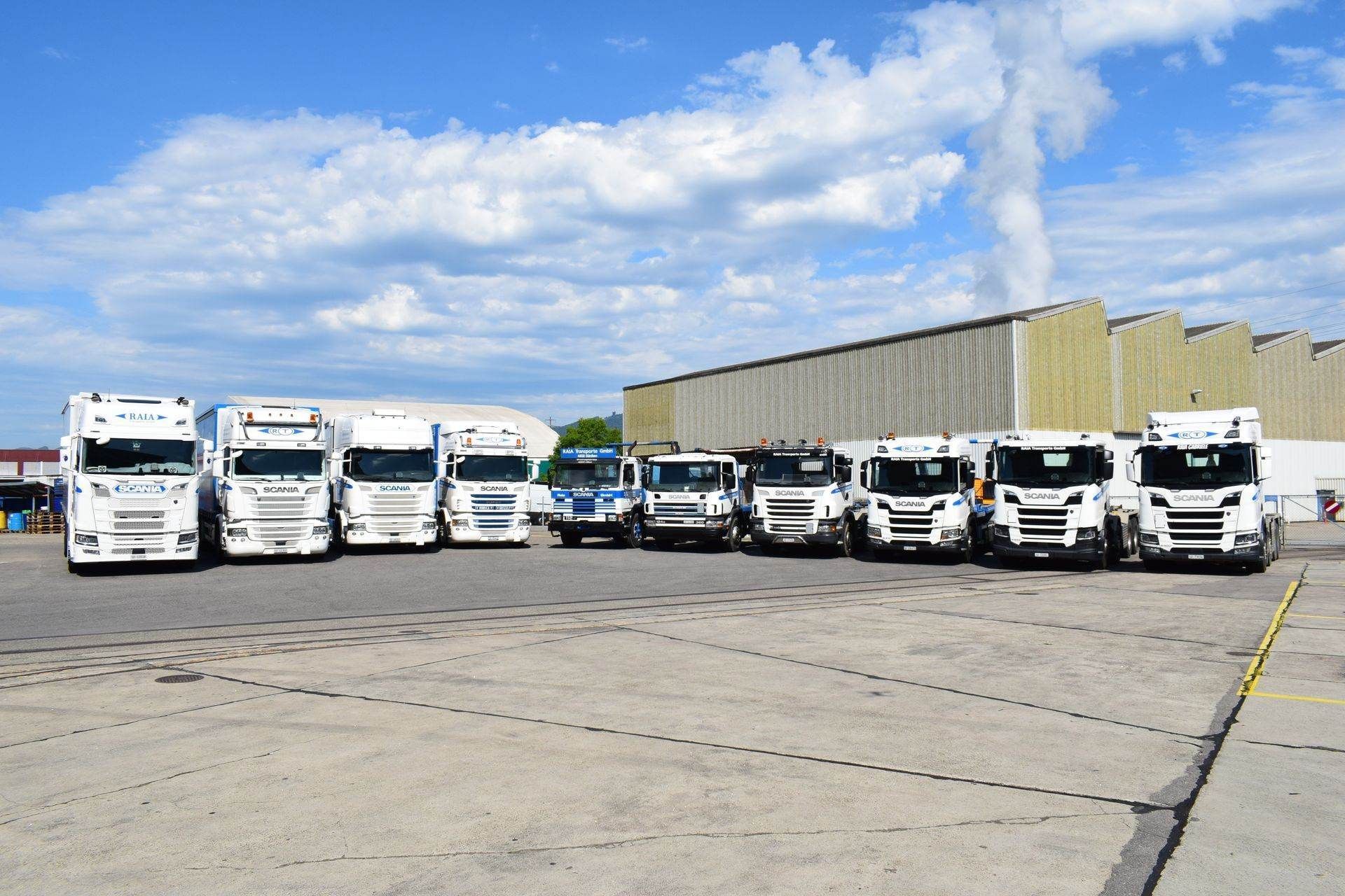 Eine Reihe weisser Sattelschlepper parkte auf einem Betonparkplatz unter einem bewölkten blauen Himmel.