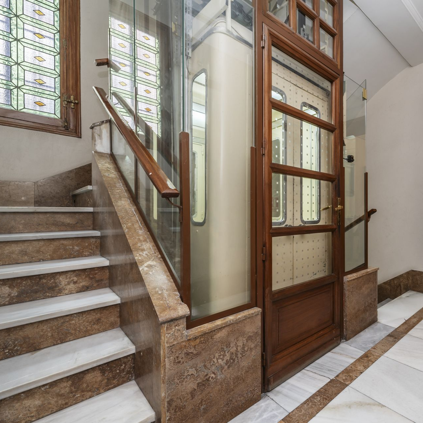 Ascenseur à côté d'un escalier avec marches en marbre et boiseries.