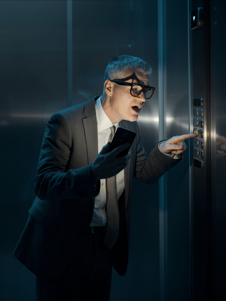Un homme en costume appuie avec impatience sur le bouton de l'ascenseur en panne.