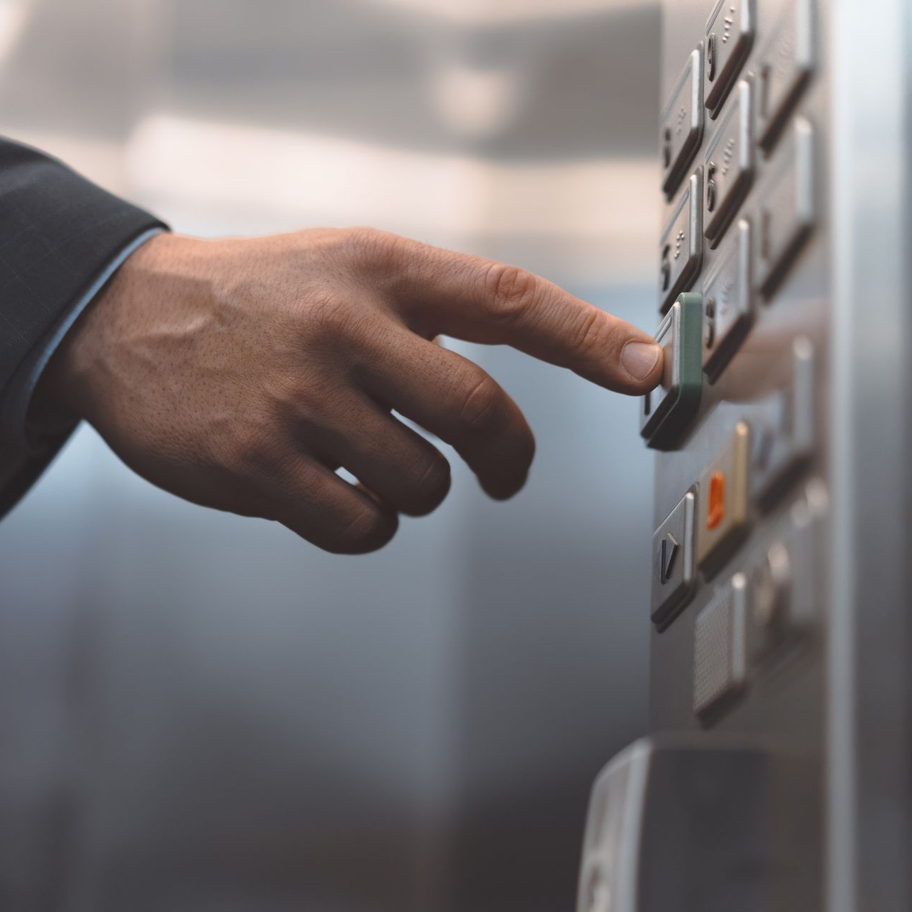 La main d'une personne portant une veste de costume appuie sur un bouton d'ascenseur.