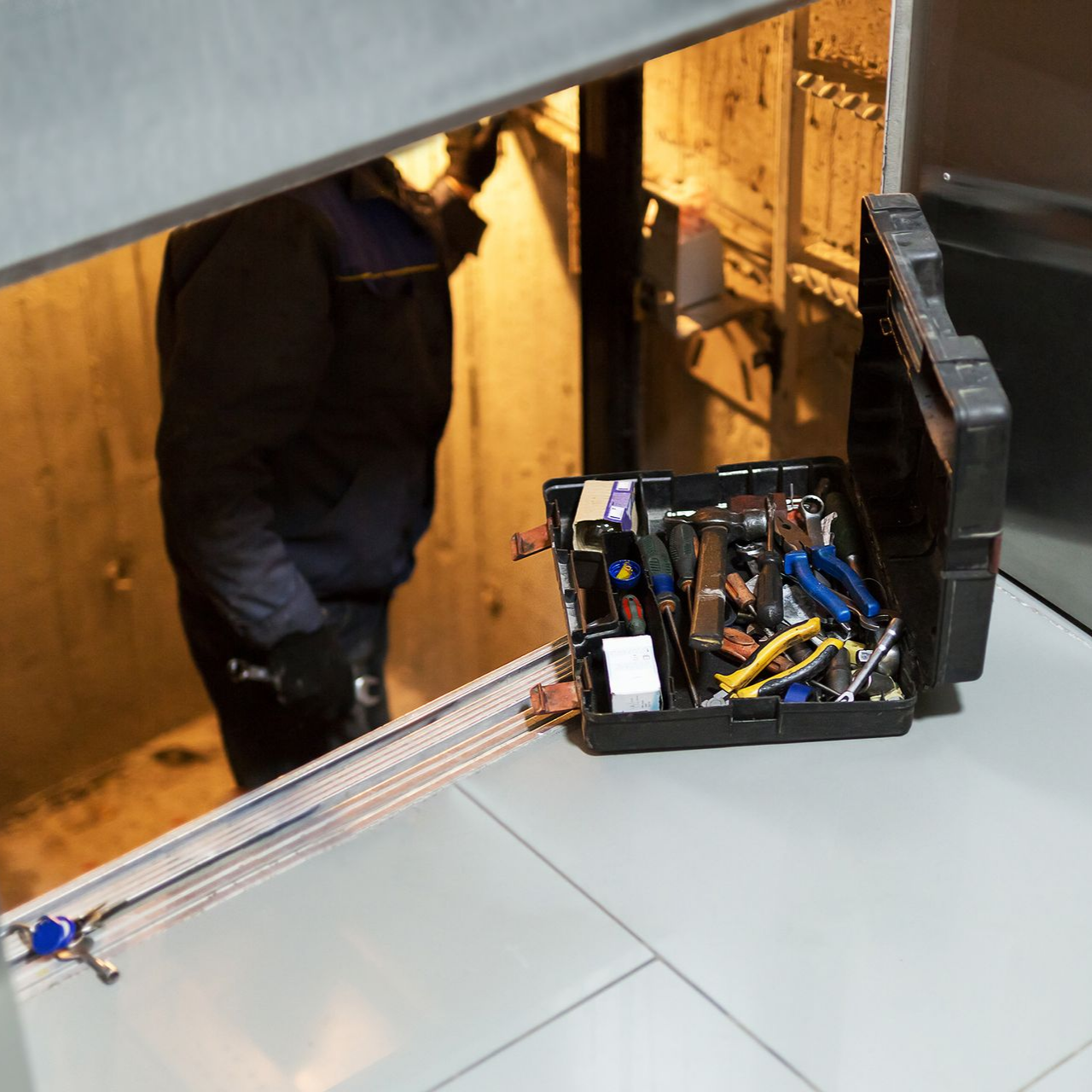 Boîte à outils ouverte avec des outils près d'une porte ; un ouvrier travaille à l'intérieur.
