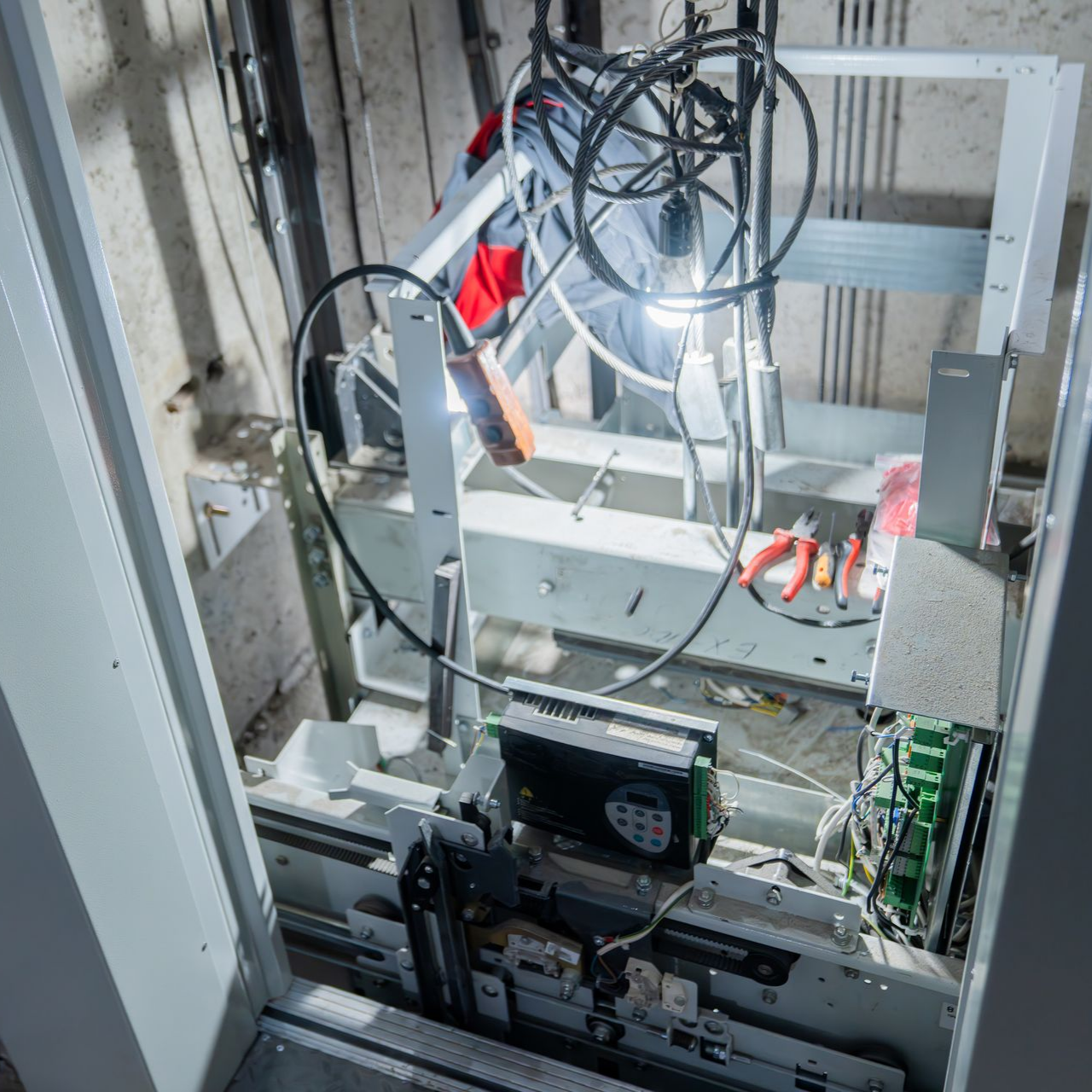 Machinerie d'ascenseur exposée ; outils et fils présents lors de la réparation.