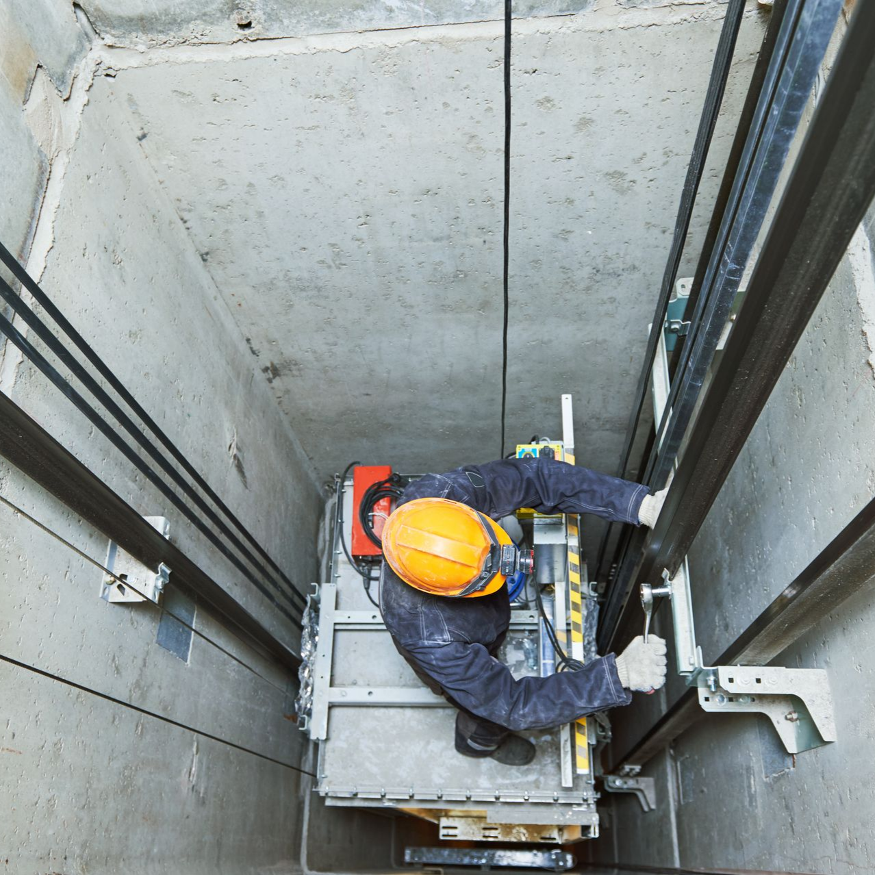 Technicien de réparation d'ascenseur dans une cage d'ascenseur, portant un casque de sécurité, inspectant les machines.