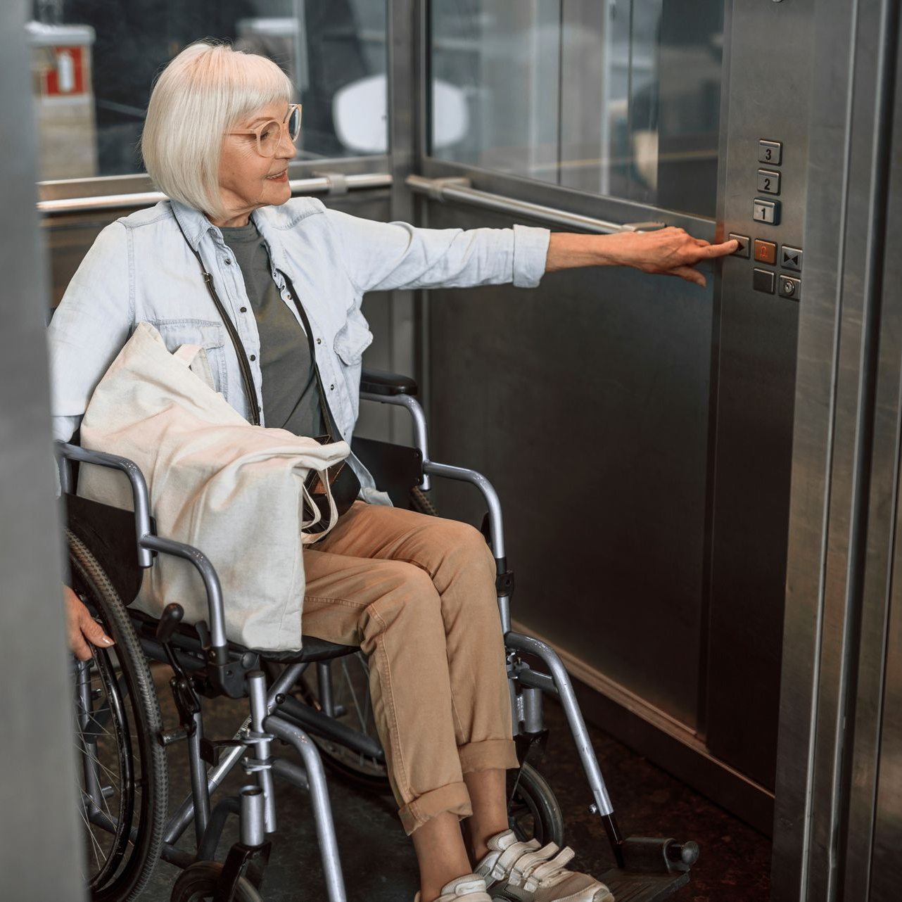 Une femme en fauteuil roulant appuie sur le bouton de l'ascenseur.