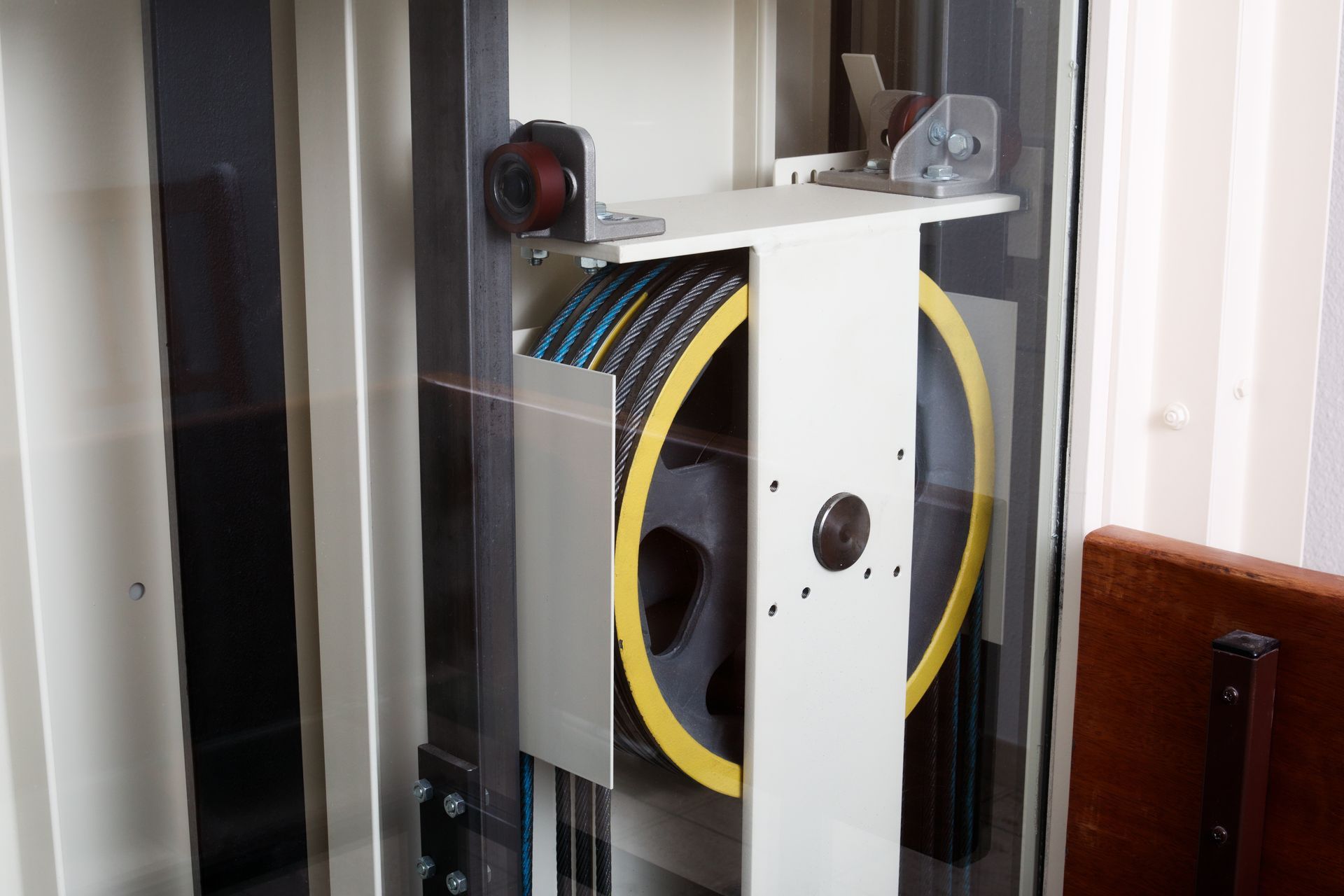 Machine d'ascenseur avec une grande poulie jaune et plusieurs câbles à l'intérieur d'un cadre métallique.