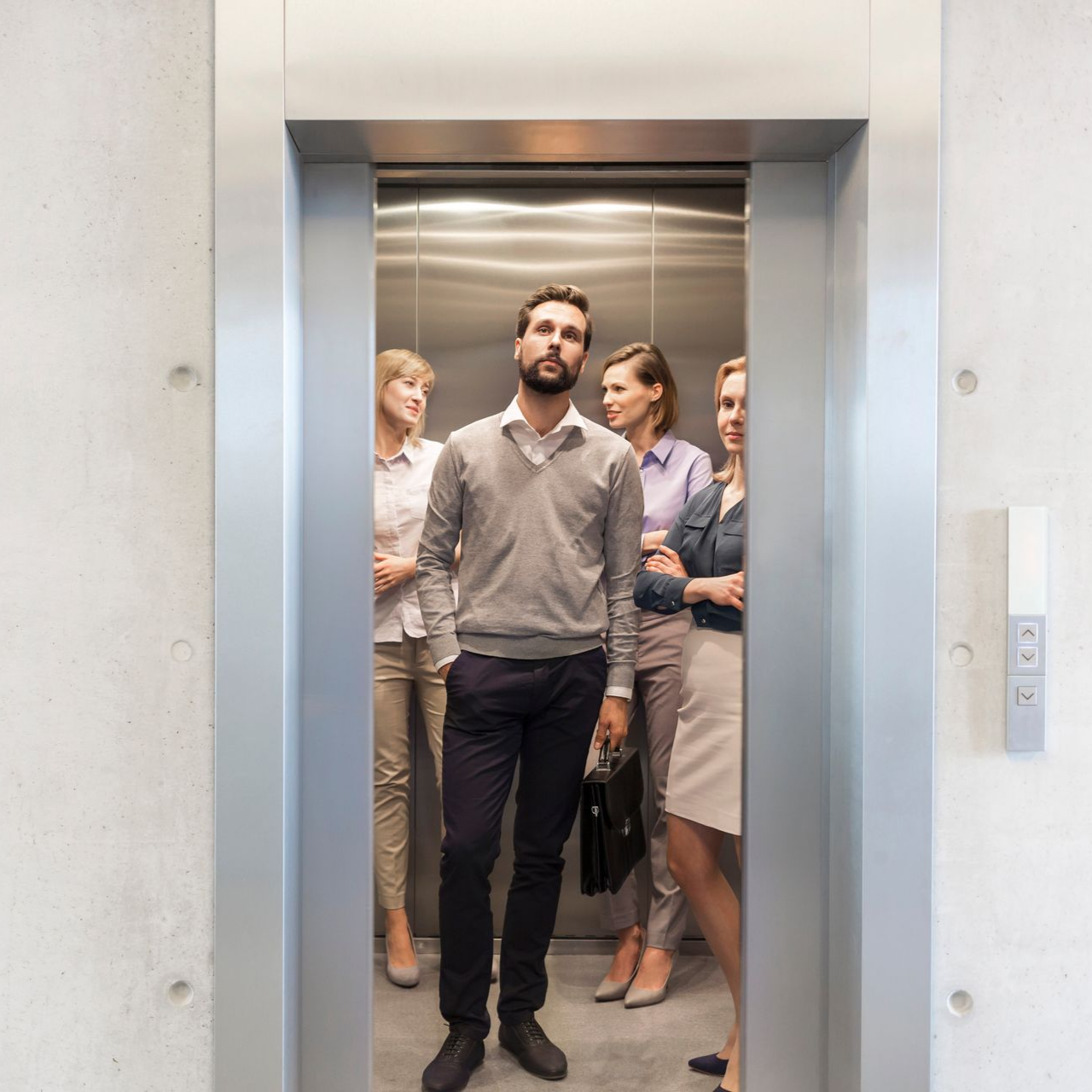 Un homme dans l'ascenseur avec trois femmes qui se tiennent derrière lui dans un ascenseur.