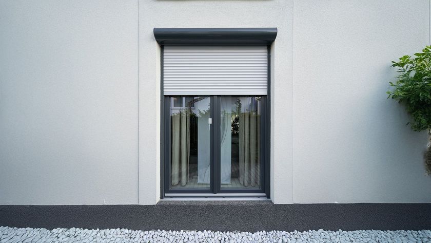 Fenêtre aux volets gris fermés, fenêtre à double vitrage avec rideaux couleur crème, encastrée dans un mur en stuc blanc.