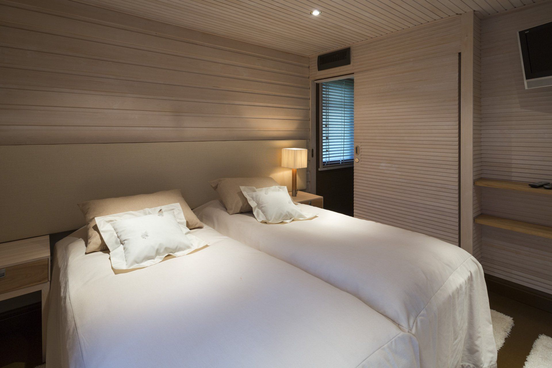 Majoitustila. Verhoiltu sängynpääty. Puinen rimaliukuovi. Pintamateriaalina vaaleaksi käsitelty paneeli. 