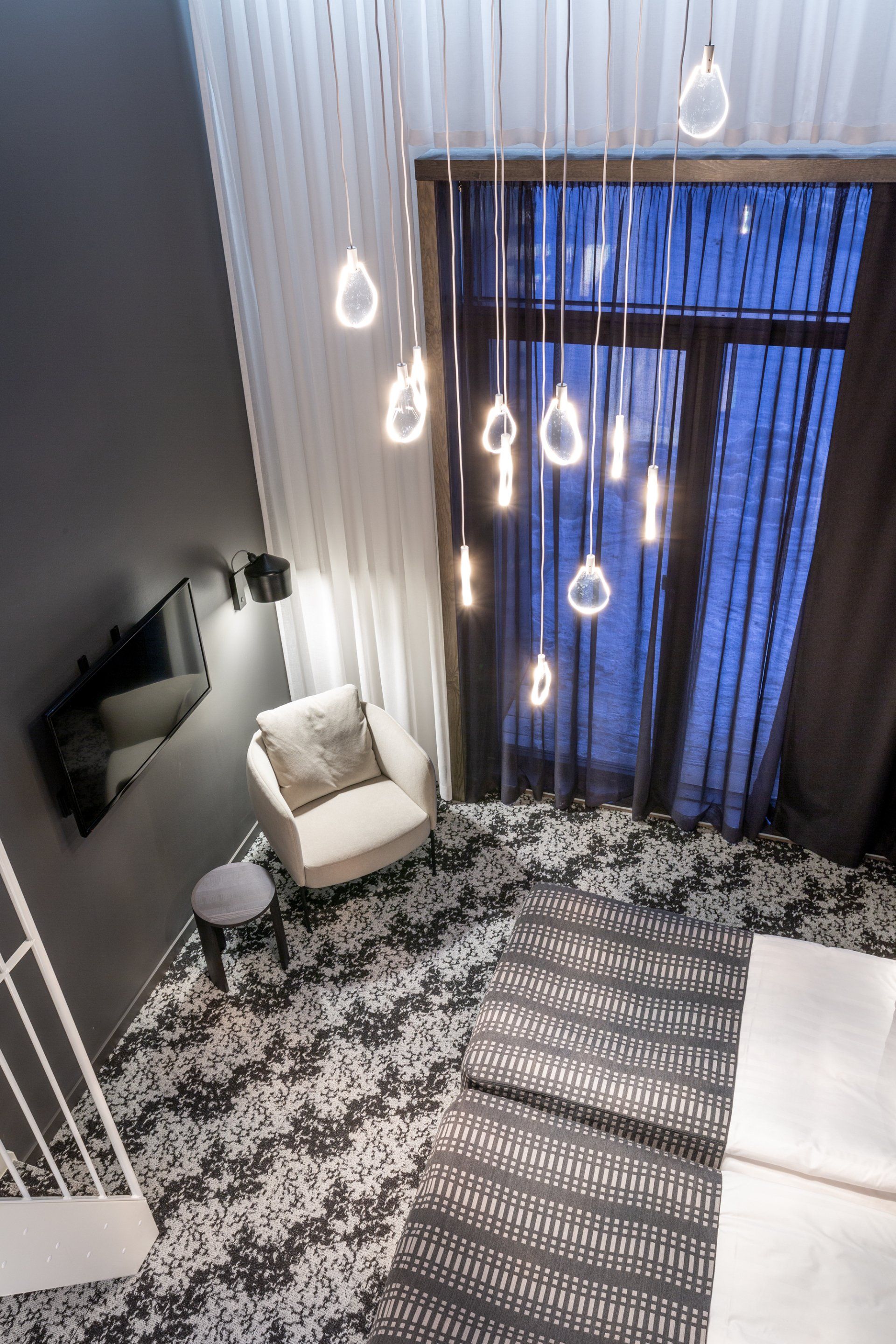 Hotellihuoneessa Saas Instruments uniikki riippuvalaisin akryylistä. Nojatuoli Adea Bonnet ja pöytä Made By Choice Airisto.