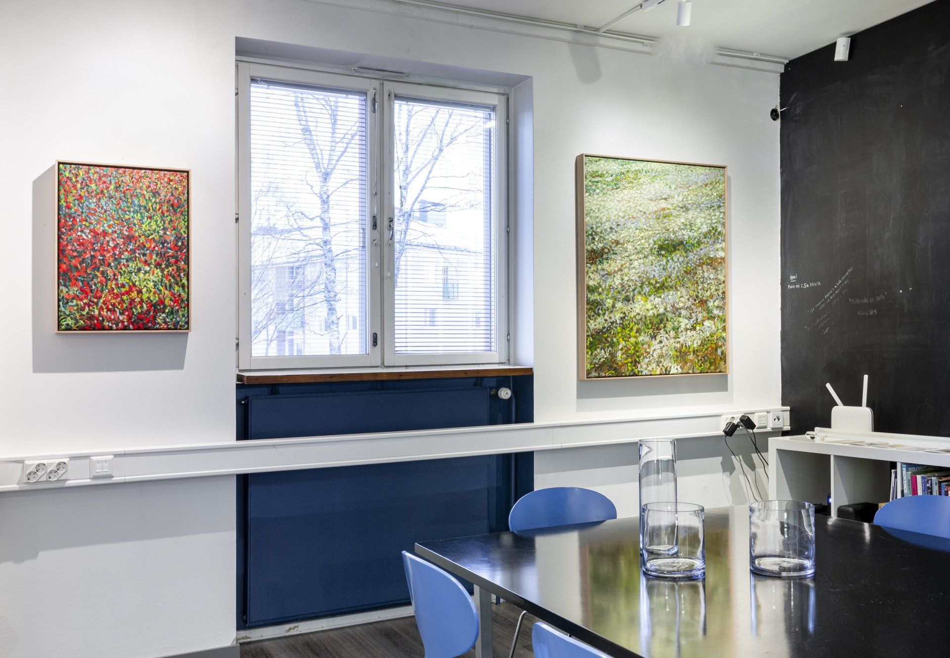 Eemil Karilan näyttely tuula y galleriassa. Neuvotteluryhmä sinisillä tuoleilla. Seinällä maalaukset. 