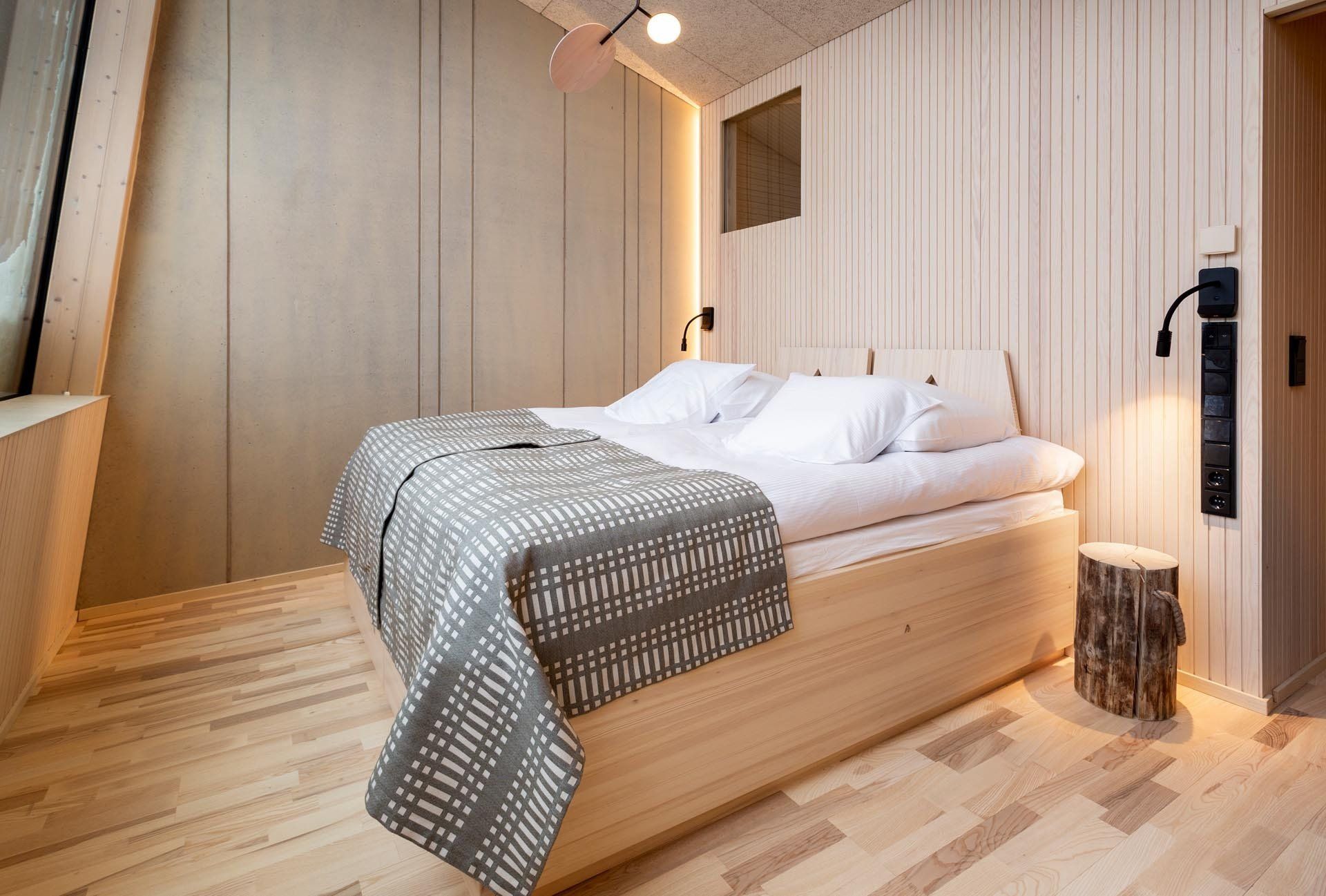 Majoitusrakennuksen makuuhuone Rovaniemellä. Puinen teetetty sänky. Päiväpeitto Johanna Gullichsen Nereus. 