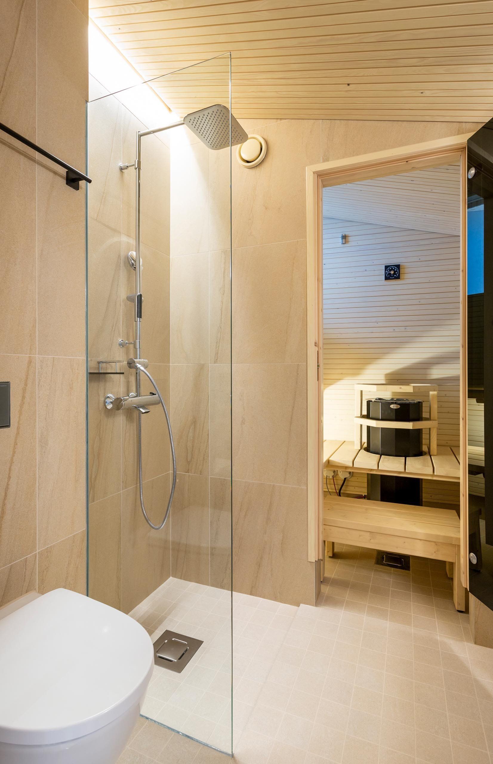 Hotellihuoneessa sauna. Musta kiuas ja havulauteet. Kylpyhuoneen seinällä beiget isot laatat. 