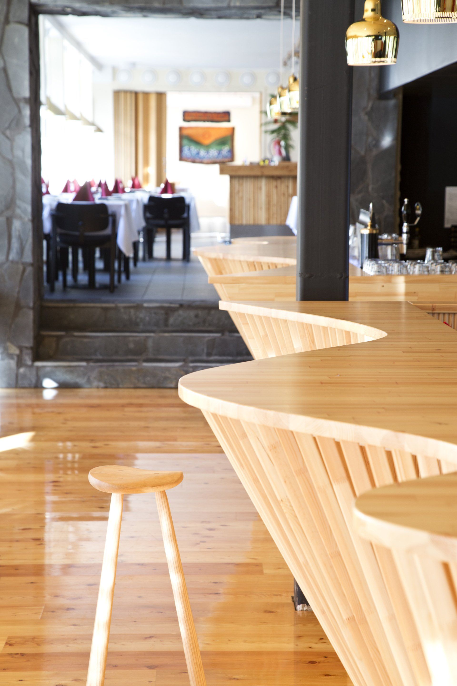 Kaareva puinen ravintolatiski puusepäntyönä. Paneloitu tiskin etupinta. Puinen taso. 