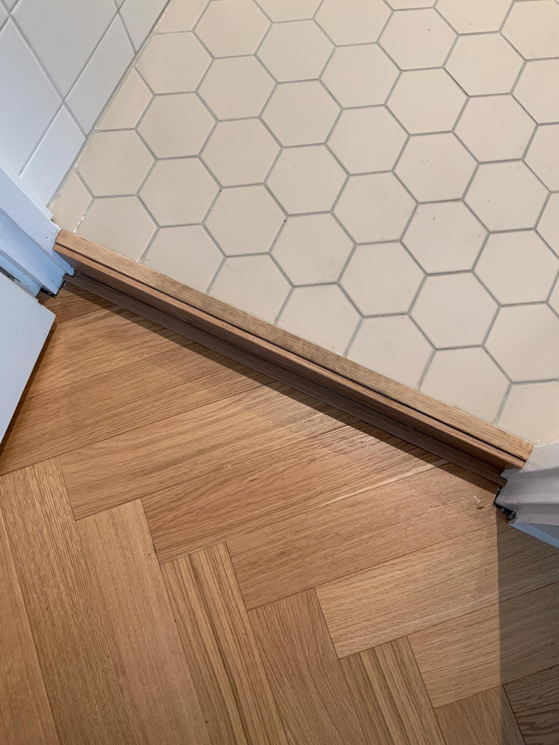 Detaljisuunnitelma - materiaalien liittymä. Kalanruotoparketti, kylpyhuoneen puukynnys ja Pukkila Natura kuuskulmalaatta.  