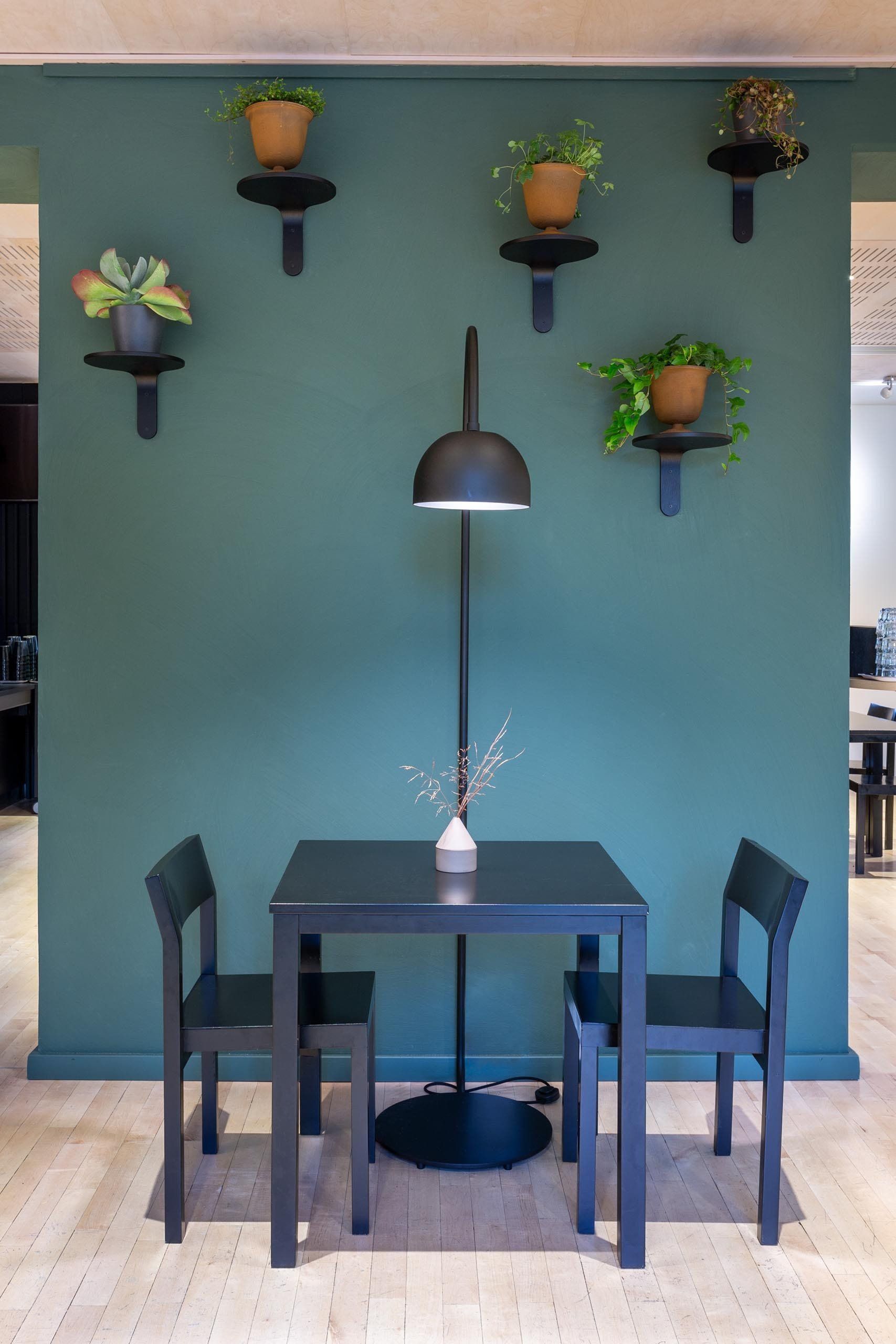 Ravintolan viherseinä. Vihreäksi maalattu seinä ja viherkasvit Muoto 2 Turn hyllyillä. Lattiavalaisin Zero Bob.