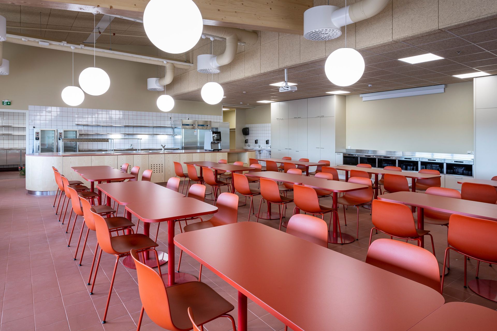 Toimitilan ruokala. Punainen lattia ja punaiset tuolit Lapalma Seela. Pöydissä punainen laminaattikansi ja laippajalka. 