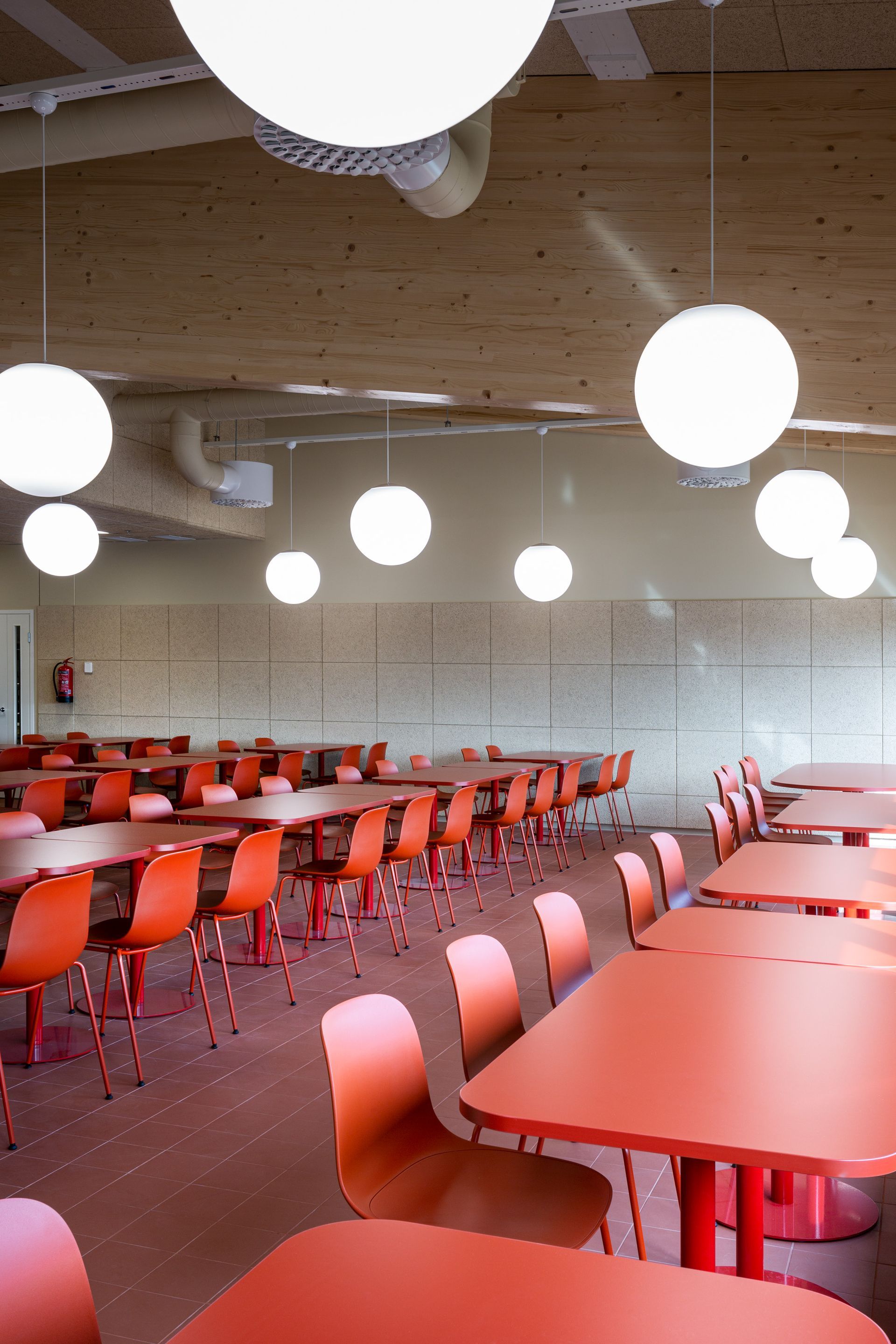 Punainen ravintolan sisustus teollisuusrakennuksessa. Riippuvat pallovalaisimet. Seinällä Hera Design akustiikkapaneelit.