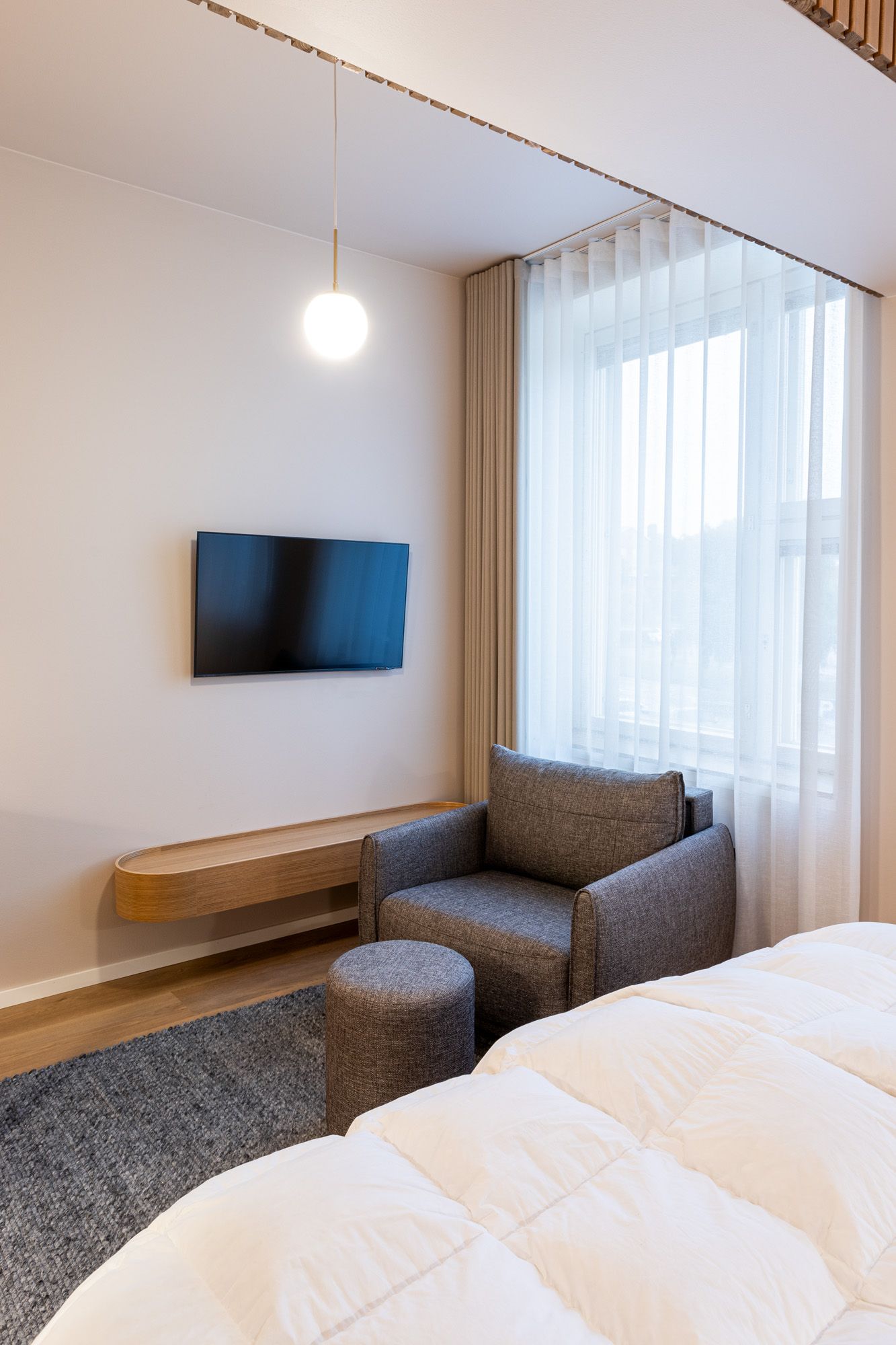Hotellihuoneen kaluste ja tekstiilisuunnittelu. Pyöristetty tv-taso puusepäntyönä. Sivu- ja valoverhoissa aaltonauha. 