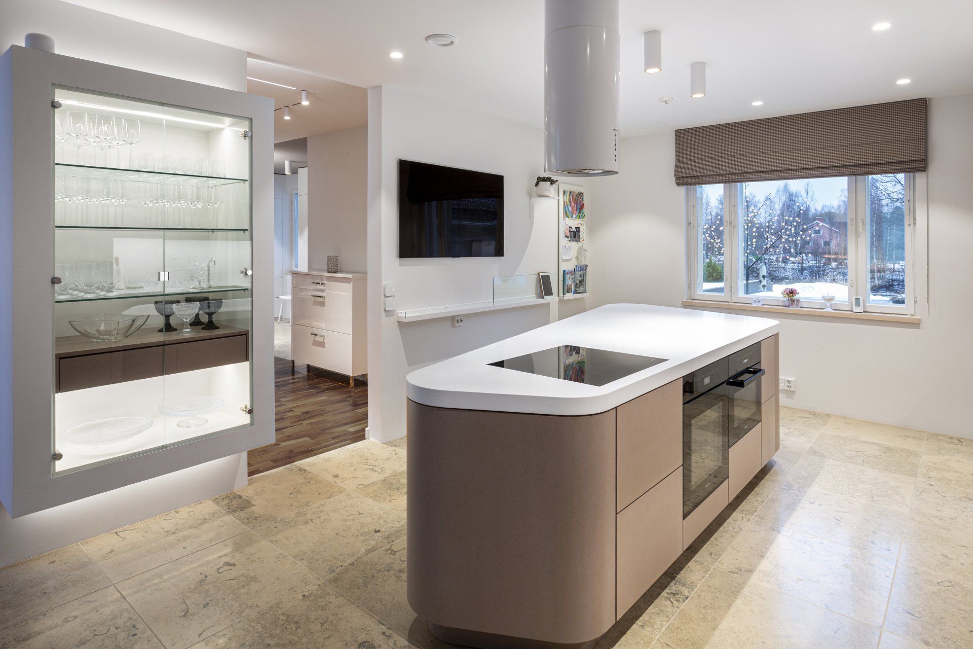 Keittiön kiintokalusteet. Veistoksellinen keittiösaareke ja valaistu lasivitriini.