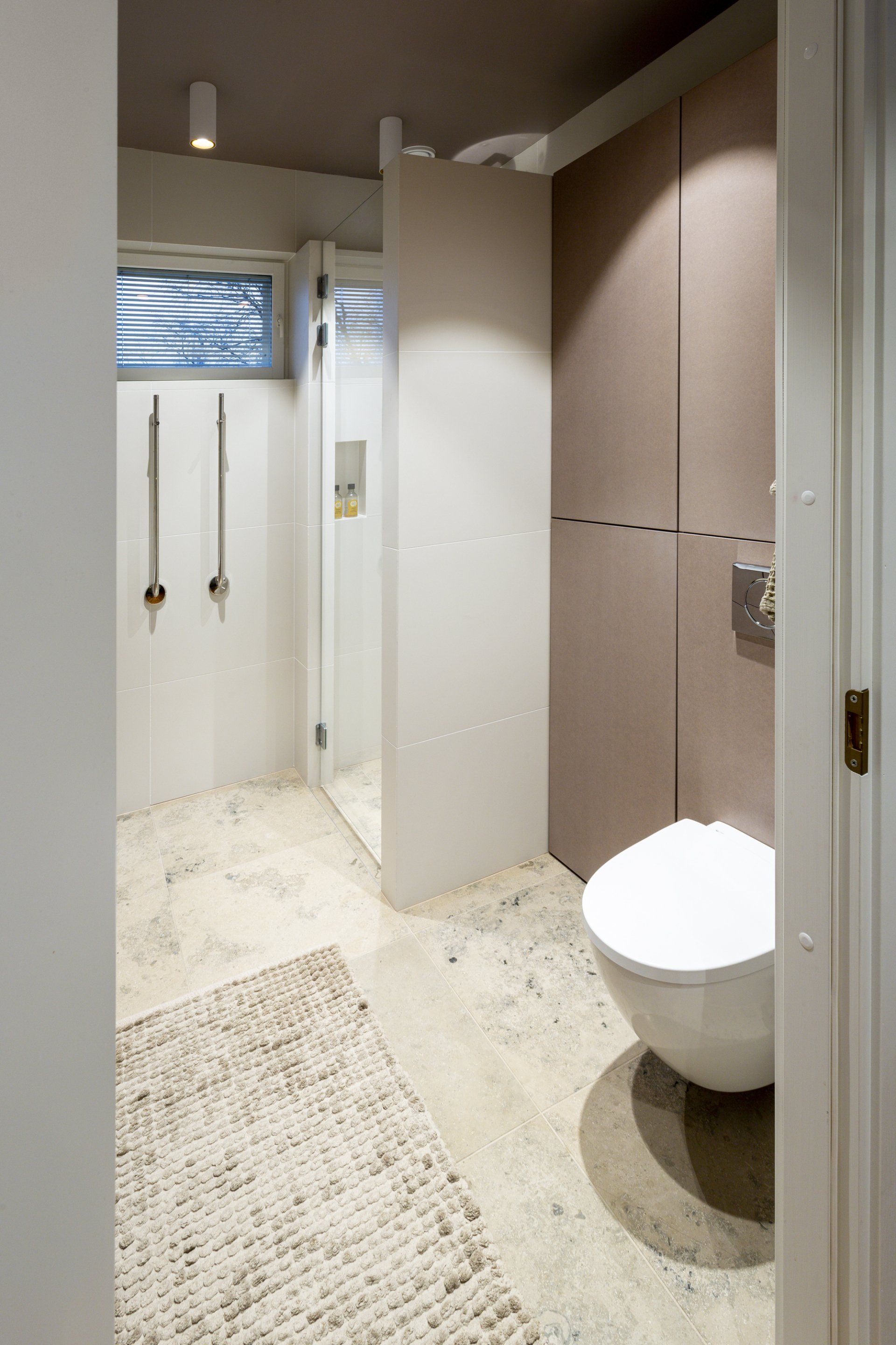 Kylpyhuoneremontti. Seinä-wc ja koteloon upotettu kylpyhuonekaluste. Lattian laatoitus kalkkikivi Tulikivi Jura Beige. 