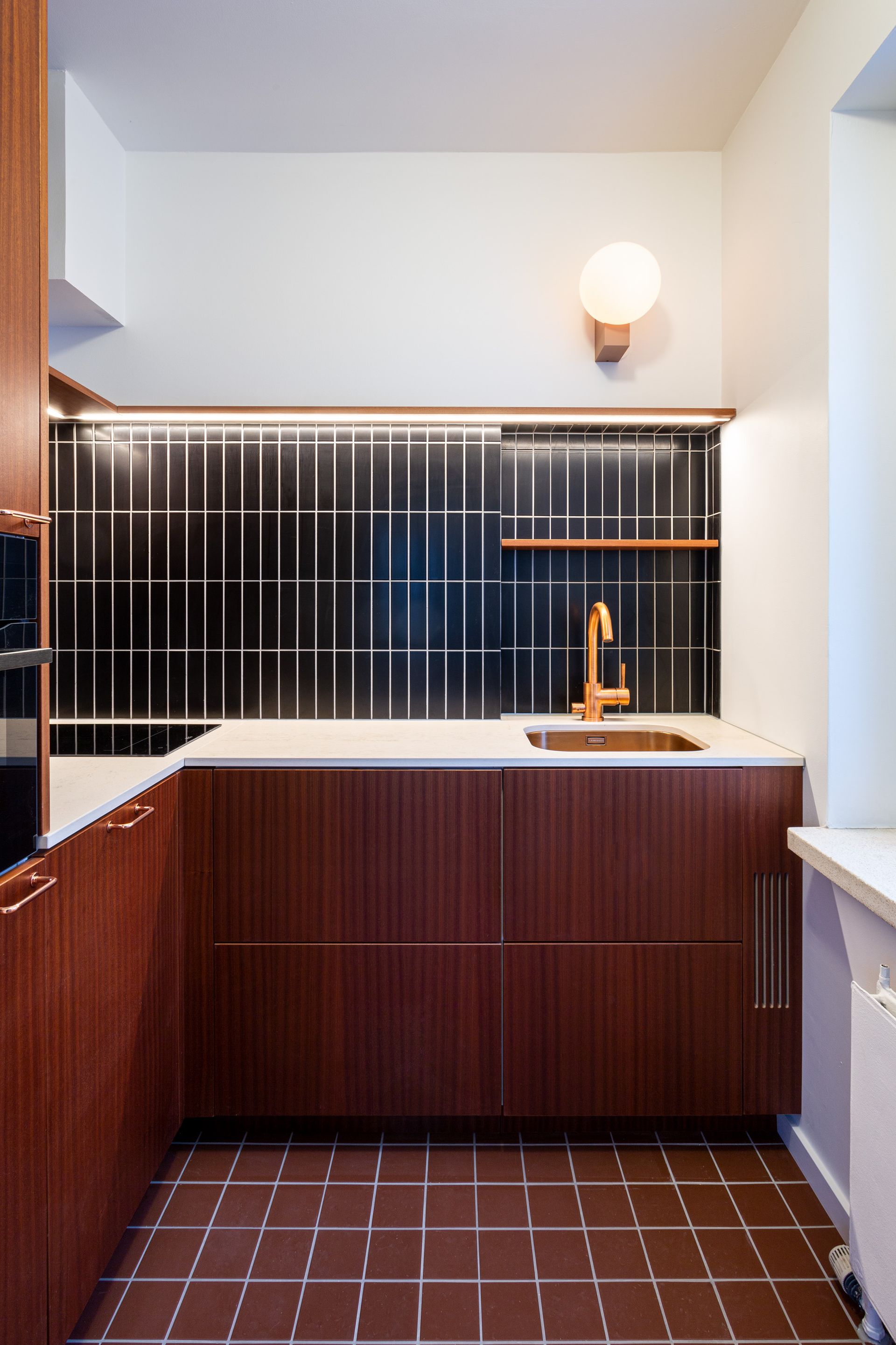 Yläkaapiton keittiö. Musta välitilalaatta ja keittiökaapit mahonkia. 