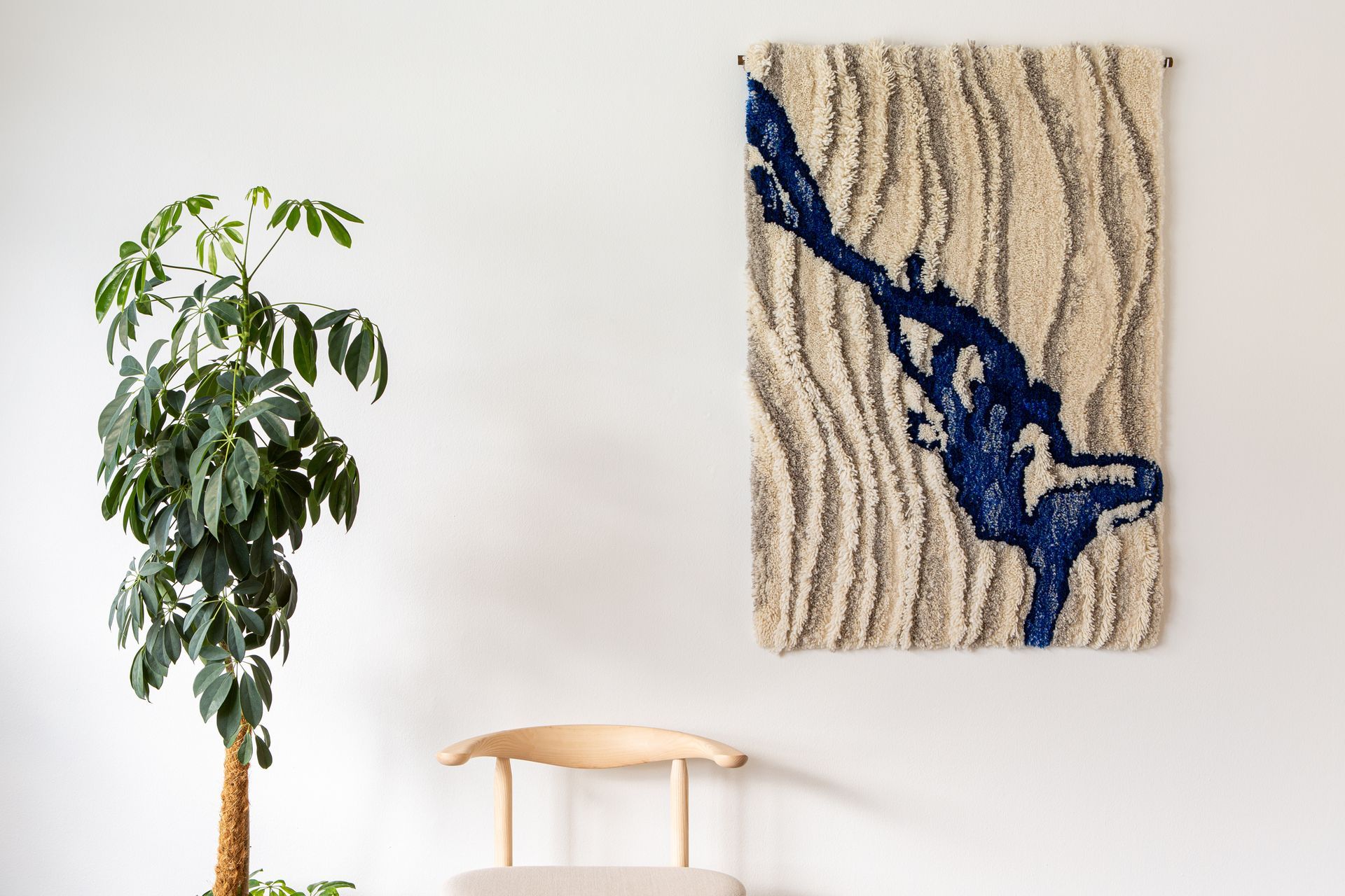 Kirsi Eskelisen ryijy seinällä. Viereen sommiteltu Nikarin puutuoli ja viherkasvi. 