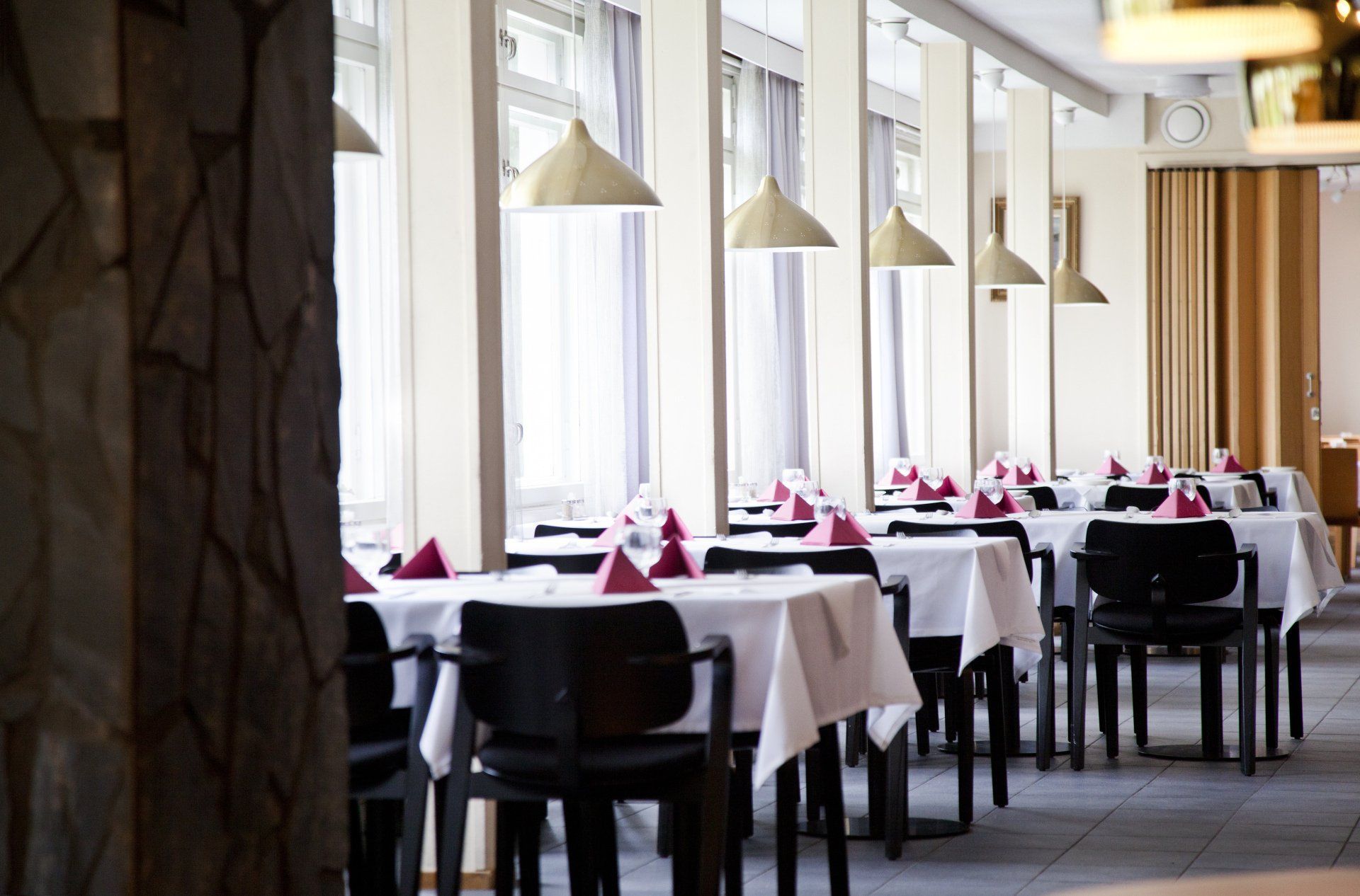 Ravintolasuunnitelma. Messinkivalaisimet. Mustat Artek Domus tuolit. Pöydällä kattaus. 