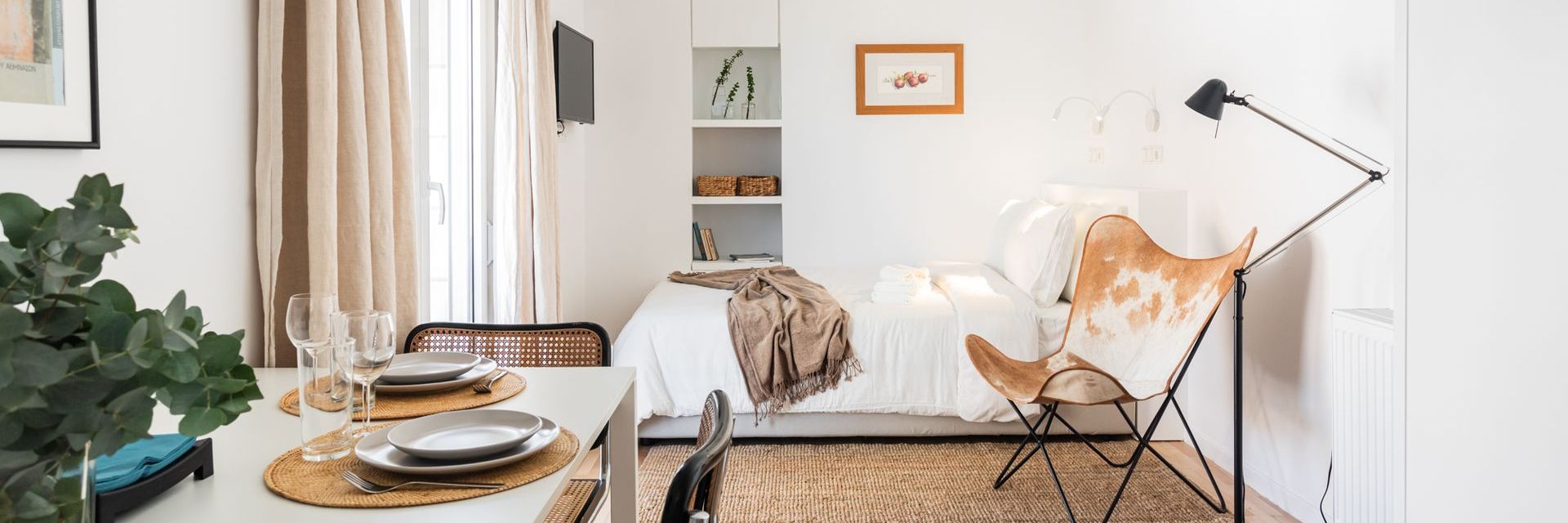 Cozy, small apartment with a table set for dinner, bed with a cowhide chair, and shelves.