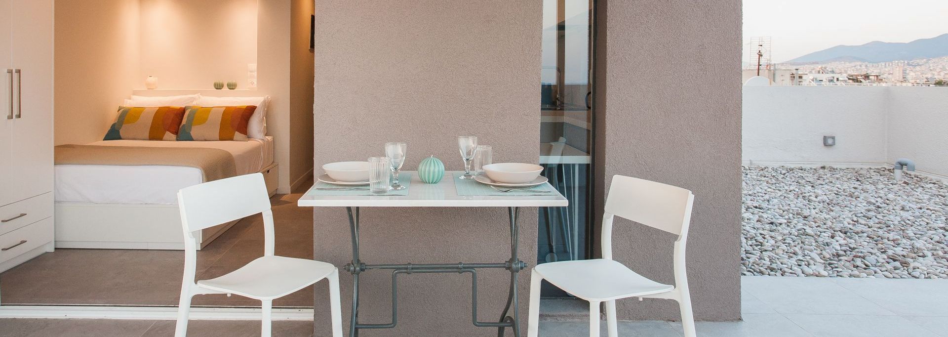 A small outdoor dining space with a table set for two and a view of a bedroom.