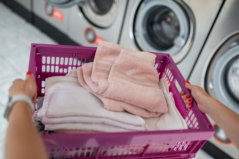 Una mujer sostiene una cesta morada llena de toallas en una lavandería.