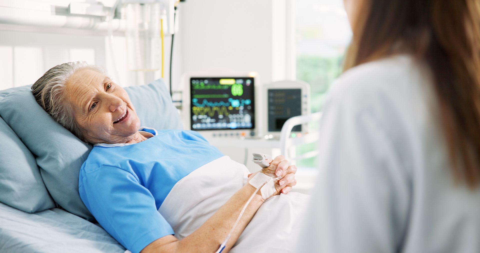 Une femme souriante dans son lit d'hôpital regarde une jeune médecin