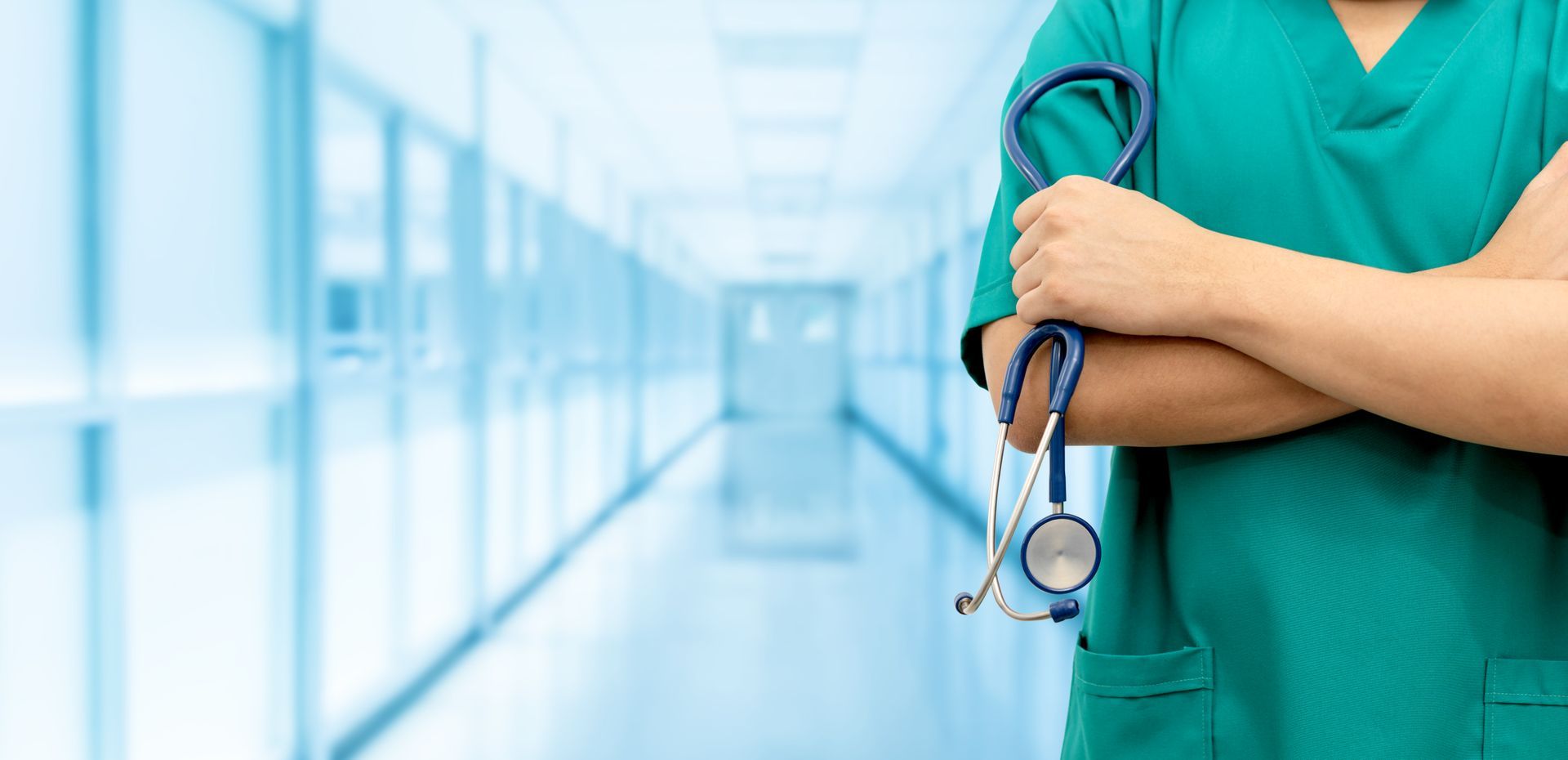 Une soignante en blouse verte, tenant un stéthoscope, dans un couloir d'hôpital lumineux