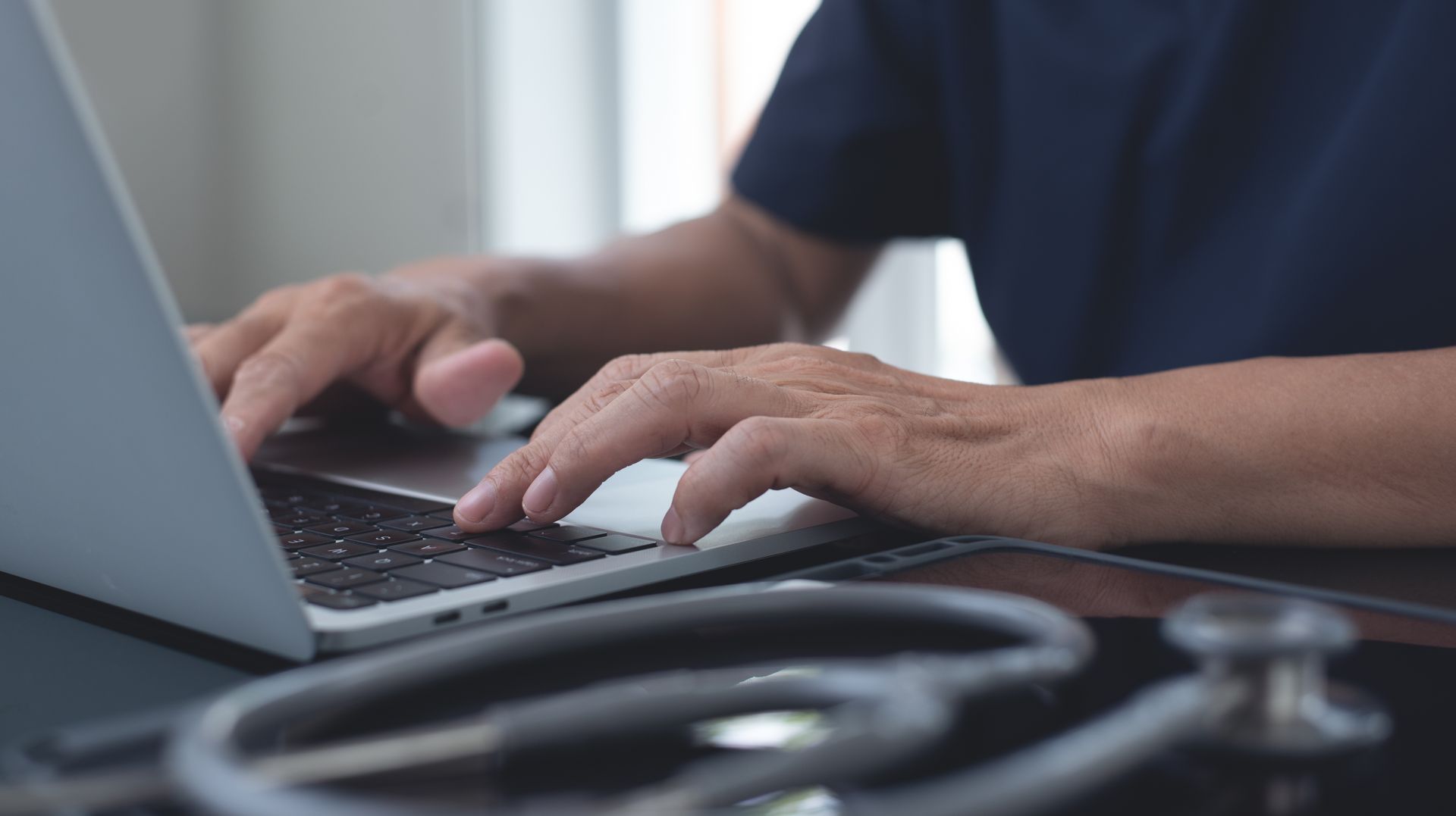 Un chirurgien qui tape à l'ordinateur, avec son stéthoscope posé à côté