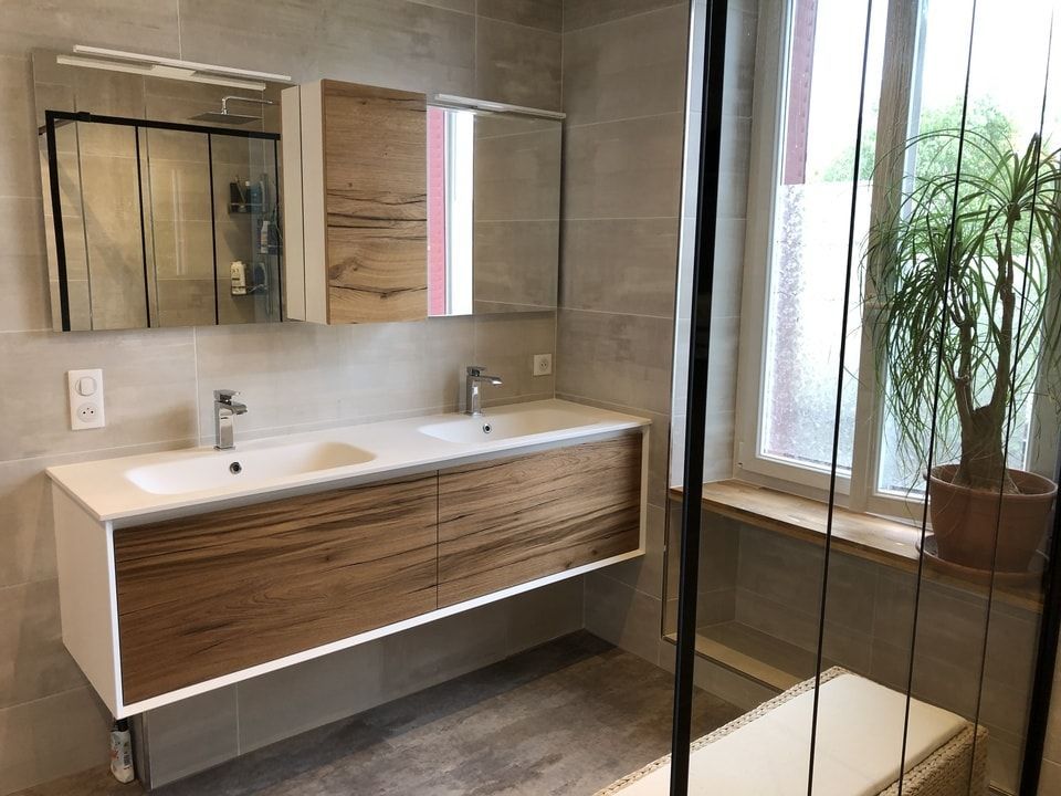 Meuble-lavabo moderne avec double vasque, grand miroir et armoires en bois, près d'une fenêtre et d'une plante en pot.