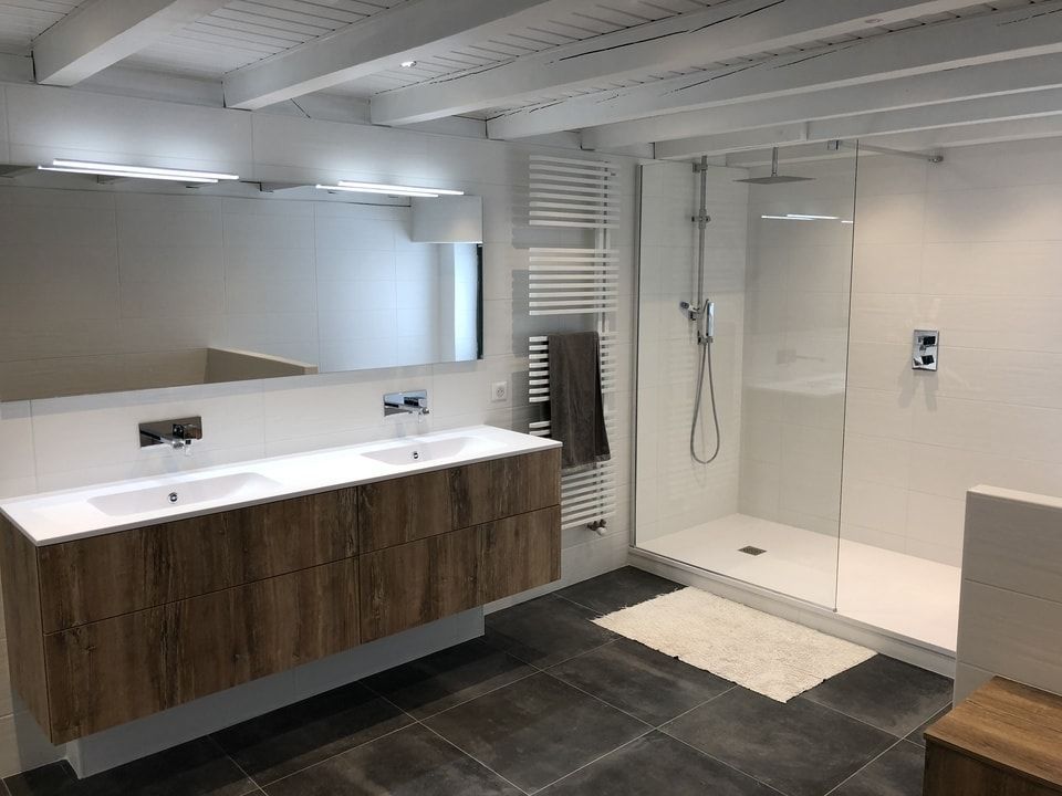 Salle de bains moderne avec meuble-lavabo double vasque, grand miroir et douche à l'italienne dans des tons blancs et boisés.