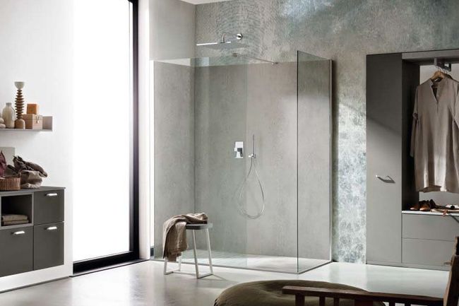 Salle de bains moderne avec une cabine de douche en verre, des murs gris et un peignoir suspendu dans un placard ouvert.