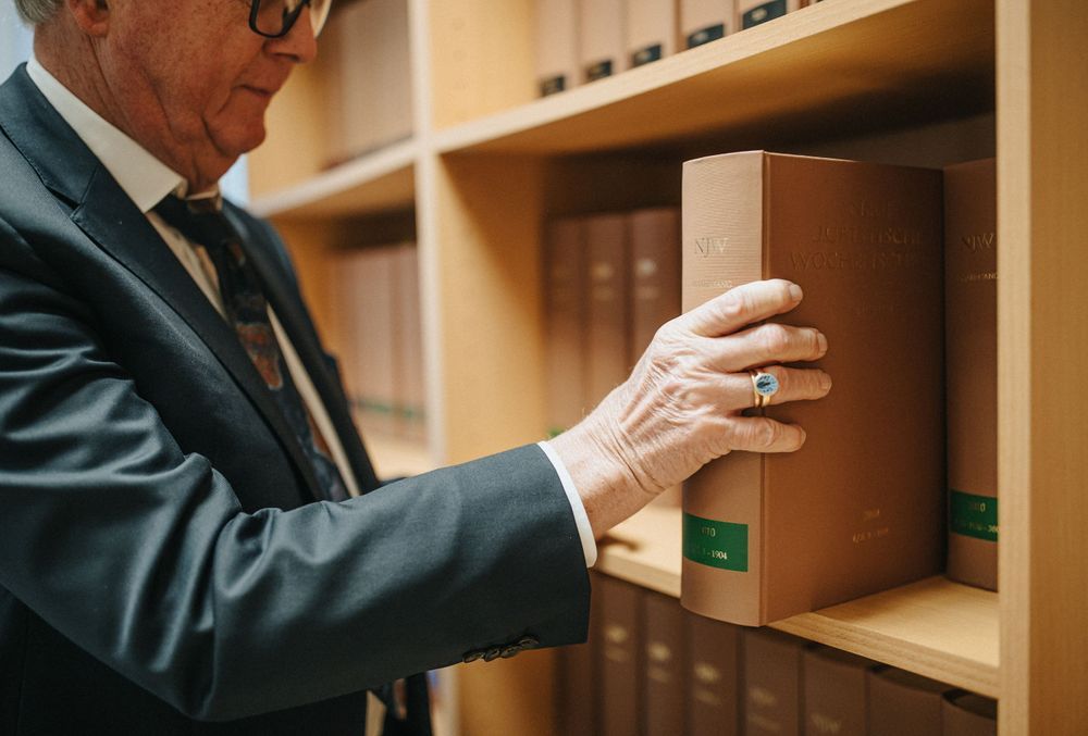 Dr. Rainer Hildebrand in Anzug und Krawatte nimmt ein Buch aus einem Bücherregal.