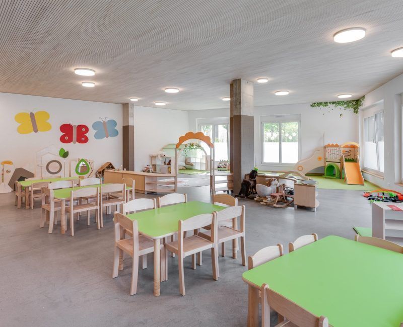 Ein großer Raum mit grünen Tischen und Stühlen und einer Rutsche.