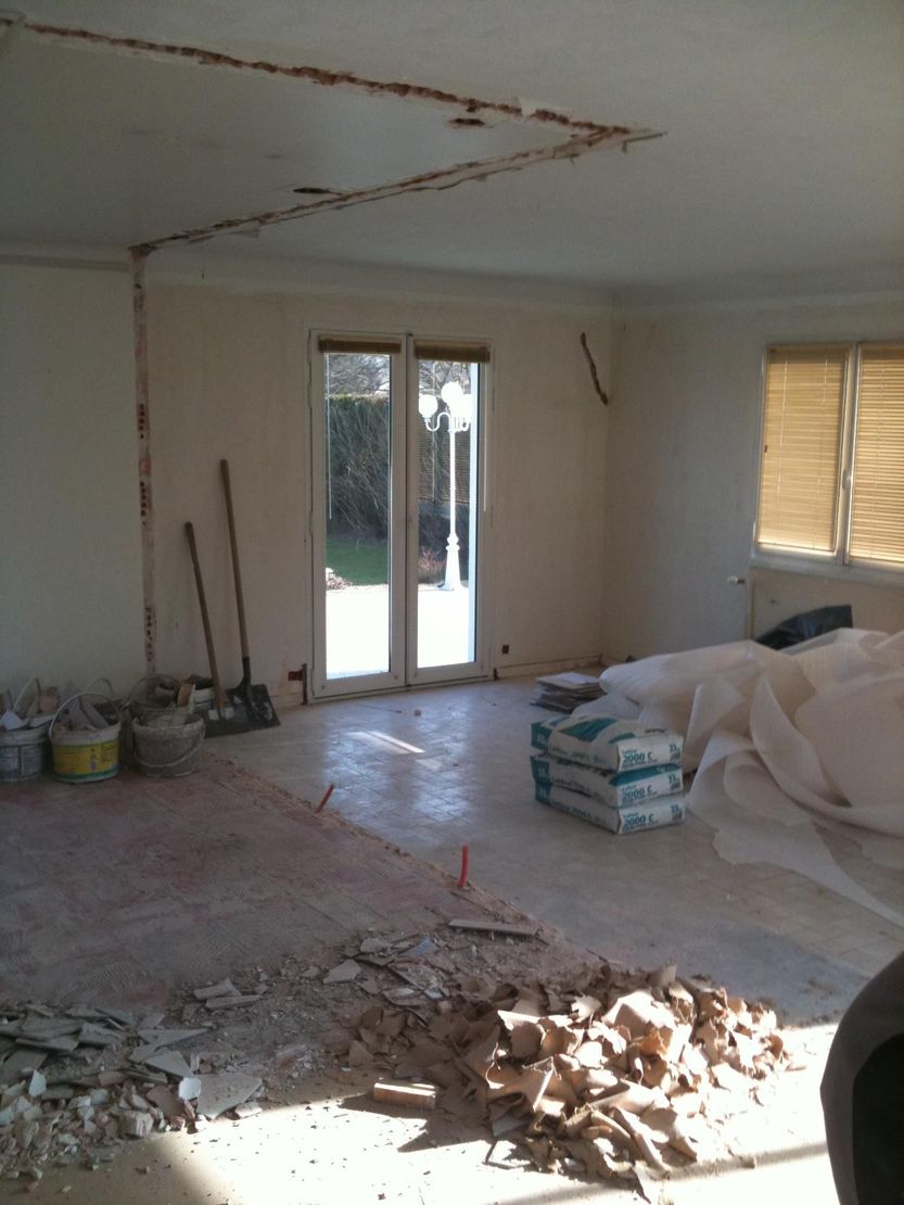 Travaux de rénovation en cours dans une pièce encombrée de débris, d'outils, de matériaux empilés et de portes vitrées doubles.