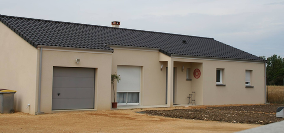 Maison beige de plain-pied avec un toit foncé, une porte de garage grise et une allée de gravier.