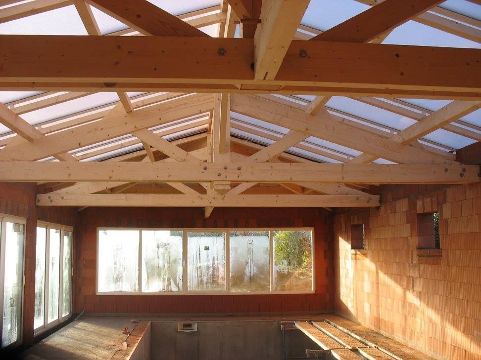 Pièce en bois vide avec poutres apparentes, grandes fenêtres et sol nu en construction.