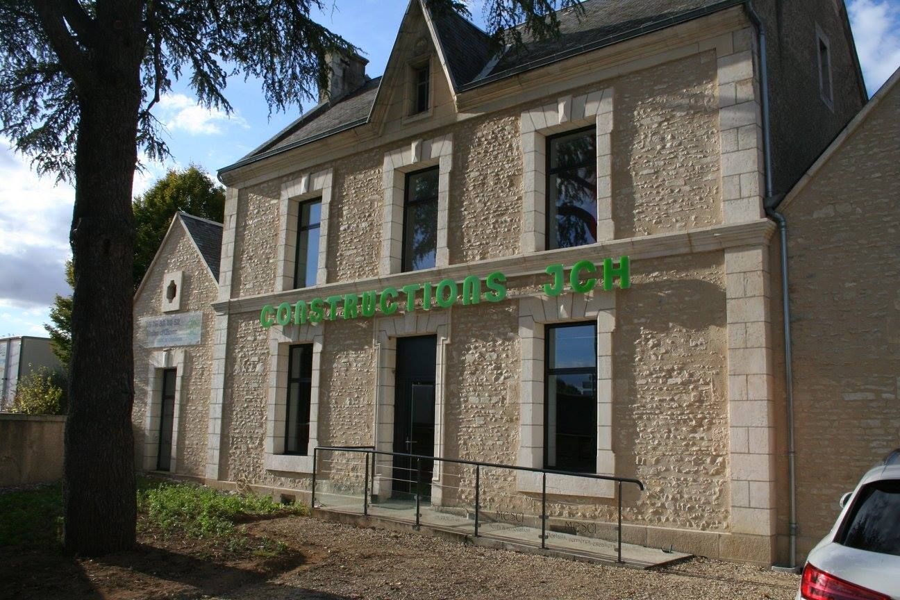 Bâtiment en pierre avec une enseigne verte, vu de l'extérieur par une journée ensoleillée.
