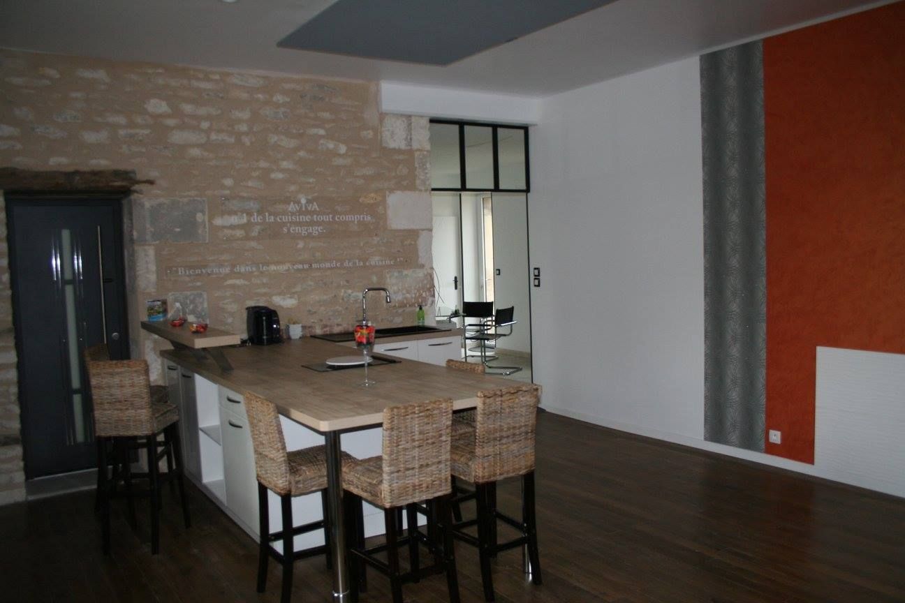Cuisine et salle à manger modernes avec îlot en briques, tabourets, sol foncé et mur d'accent orange.