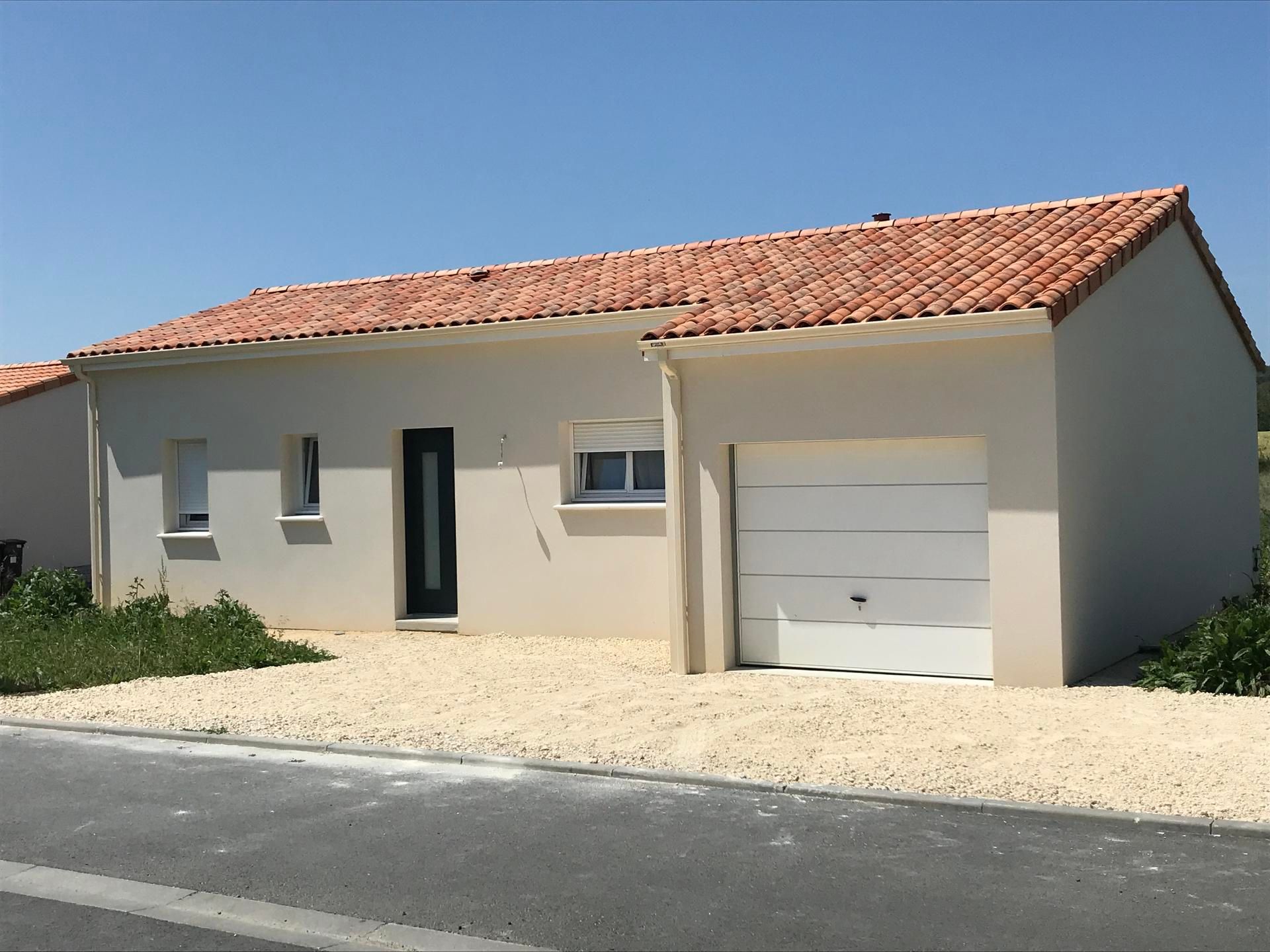 Maison de plain-pied beige avec toit de tuiles rouges, porte de garage blanche et cour avant en gravier.