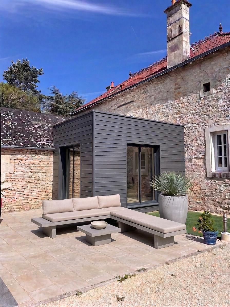 Cour en pierre avec un coin salon moderne en terrasse grise jouxtant une vieille maison en pierre.
