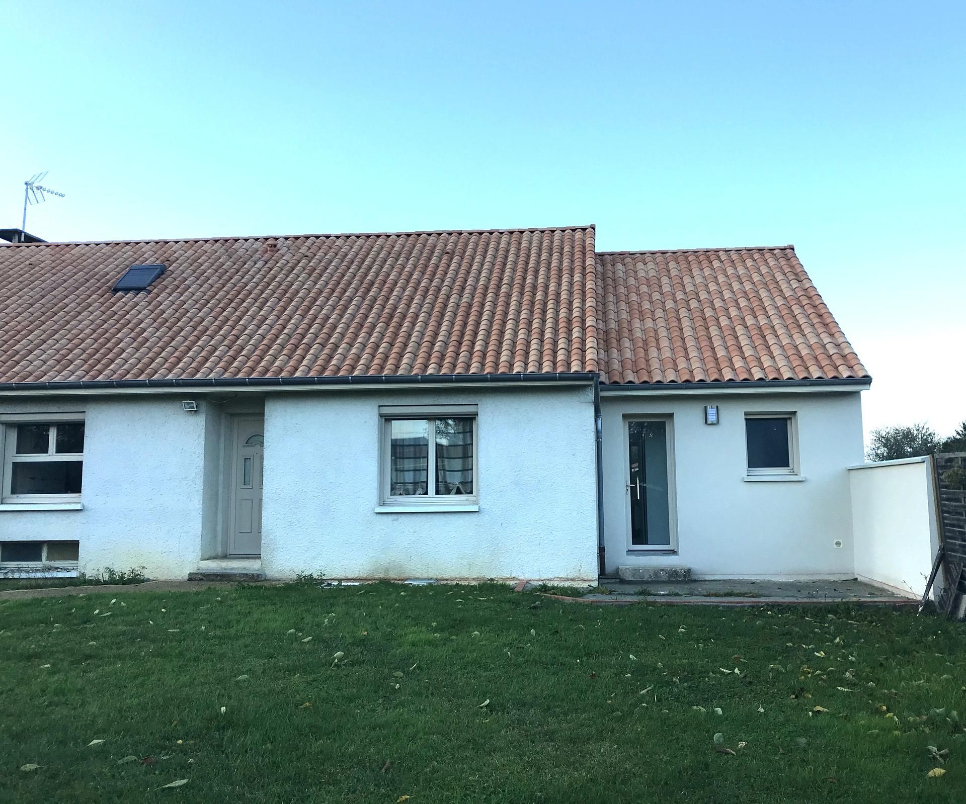 Petite maison blanche au toit de tuiles rouges et pelouse devant.