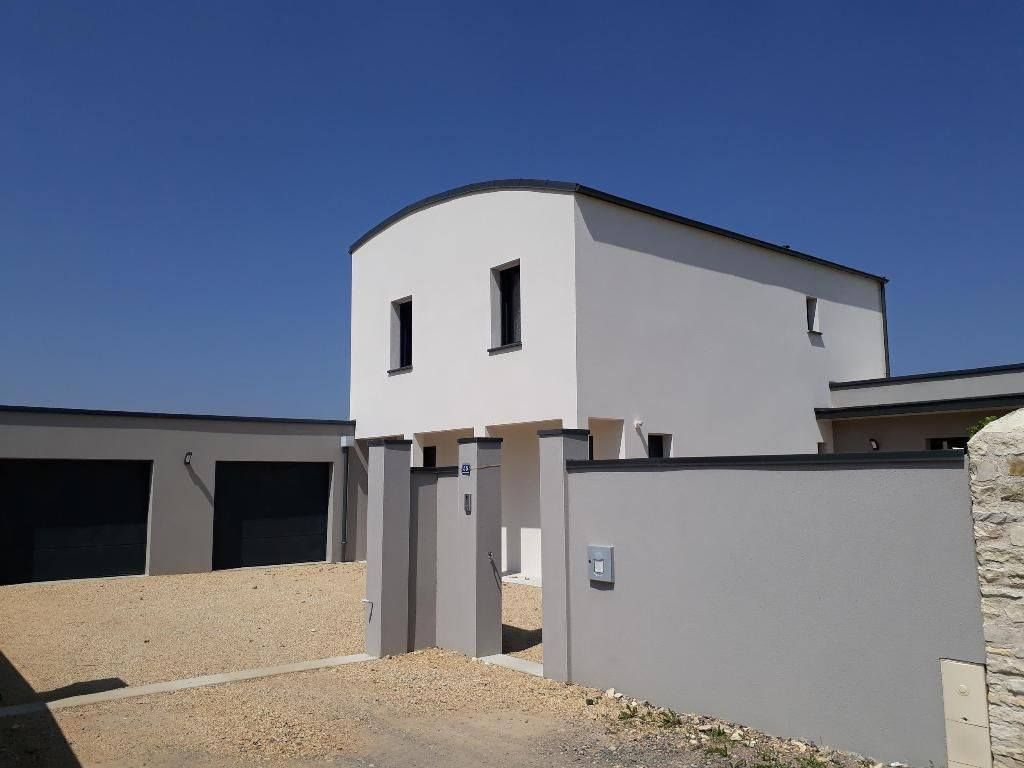Maison blanche moderne avec un mur et un portail gris sous un ciel bleu clair.