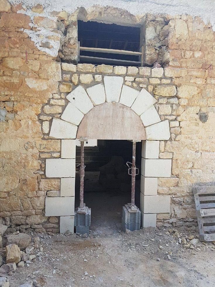 Porte en pierre avec des blocs blancs arqués dans un mur de pierre brute.