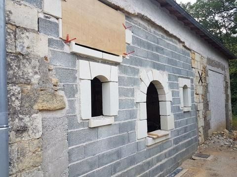 Maison en pierre en construction, avec fenêtres condamnées et ouvertures cintrées.