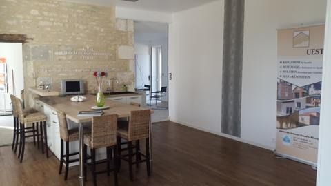 Salle à manger moderne avec table et chaises en bois, mur en pierre et plan ouvert.
